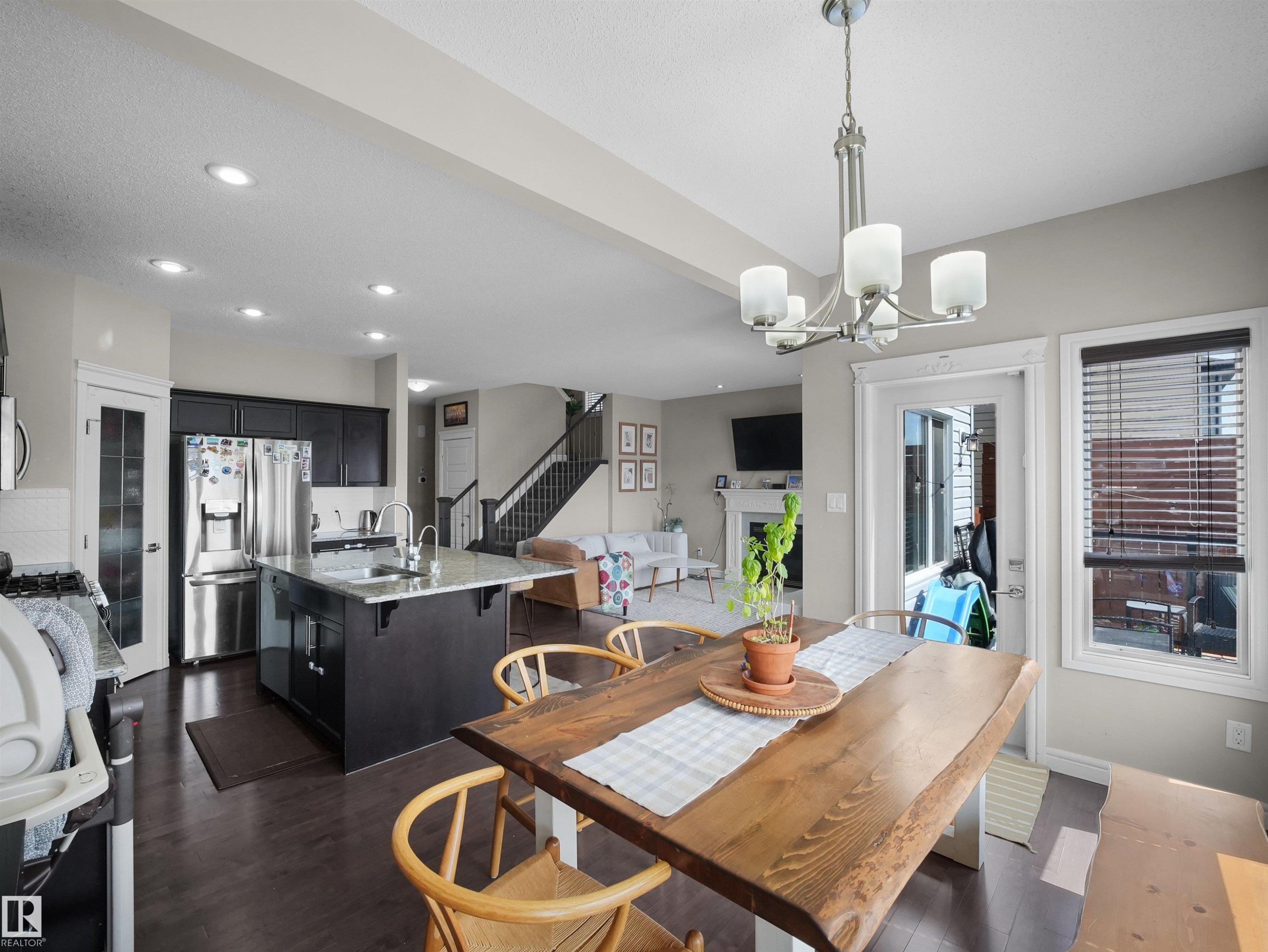 Open-concept kitchen and dining area featuring dark wood-finish flooring, a kitchen island with a light-toned countertop, dark cabinetry, and stainless steel appliances - 3247 15 Avenue Nw, Edmonton, AB