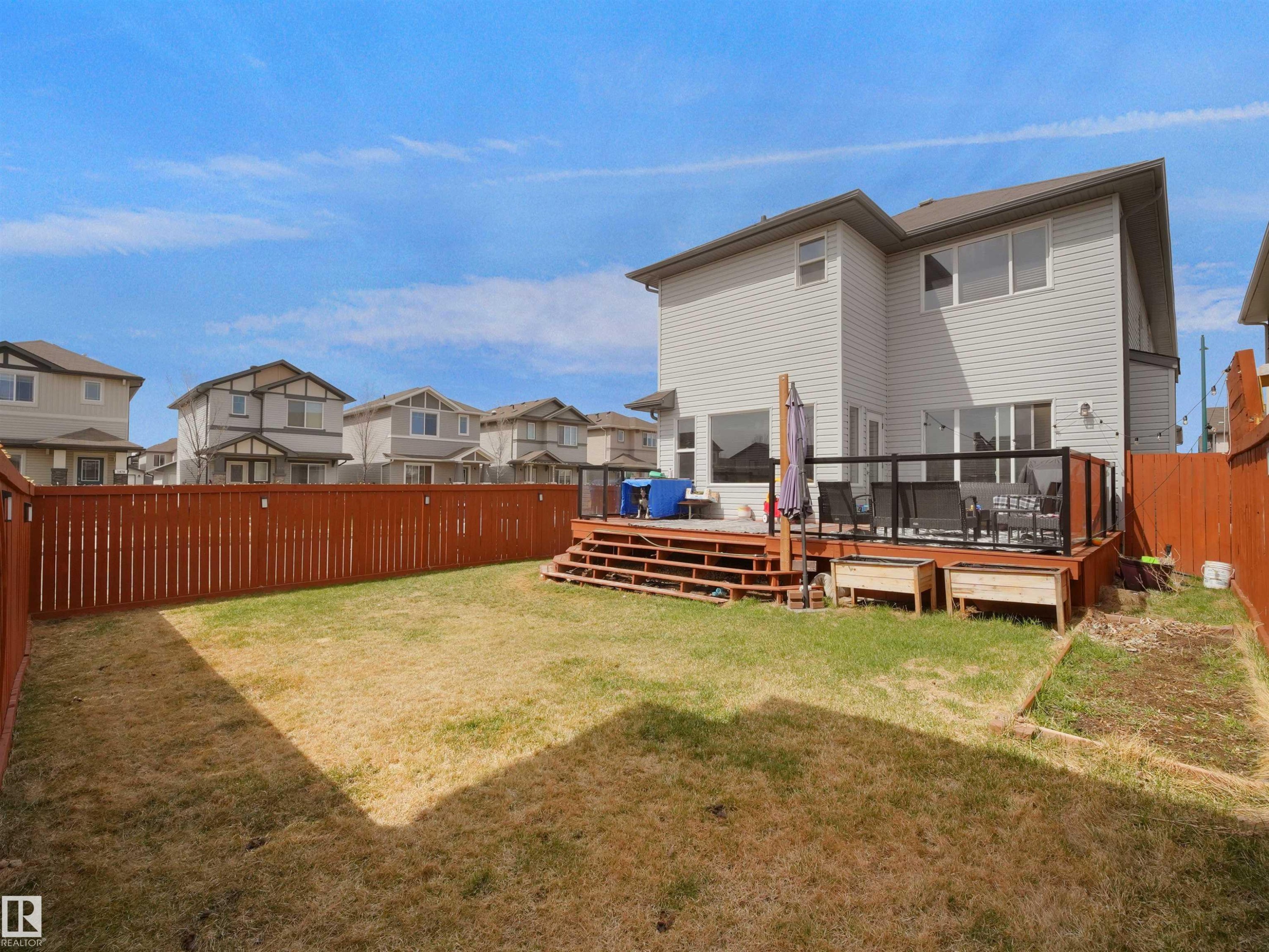 Expansive backyard featuring a multi-level wood deck with black metal and glass railings, a full privacy fence, and raised garden beds - 3247 15 Avenue Nw, Edmonton, AB