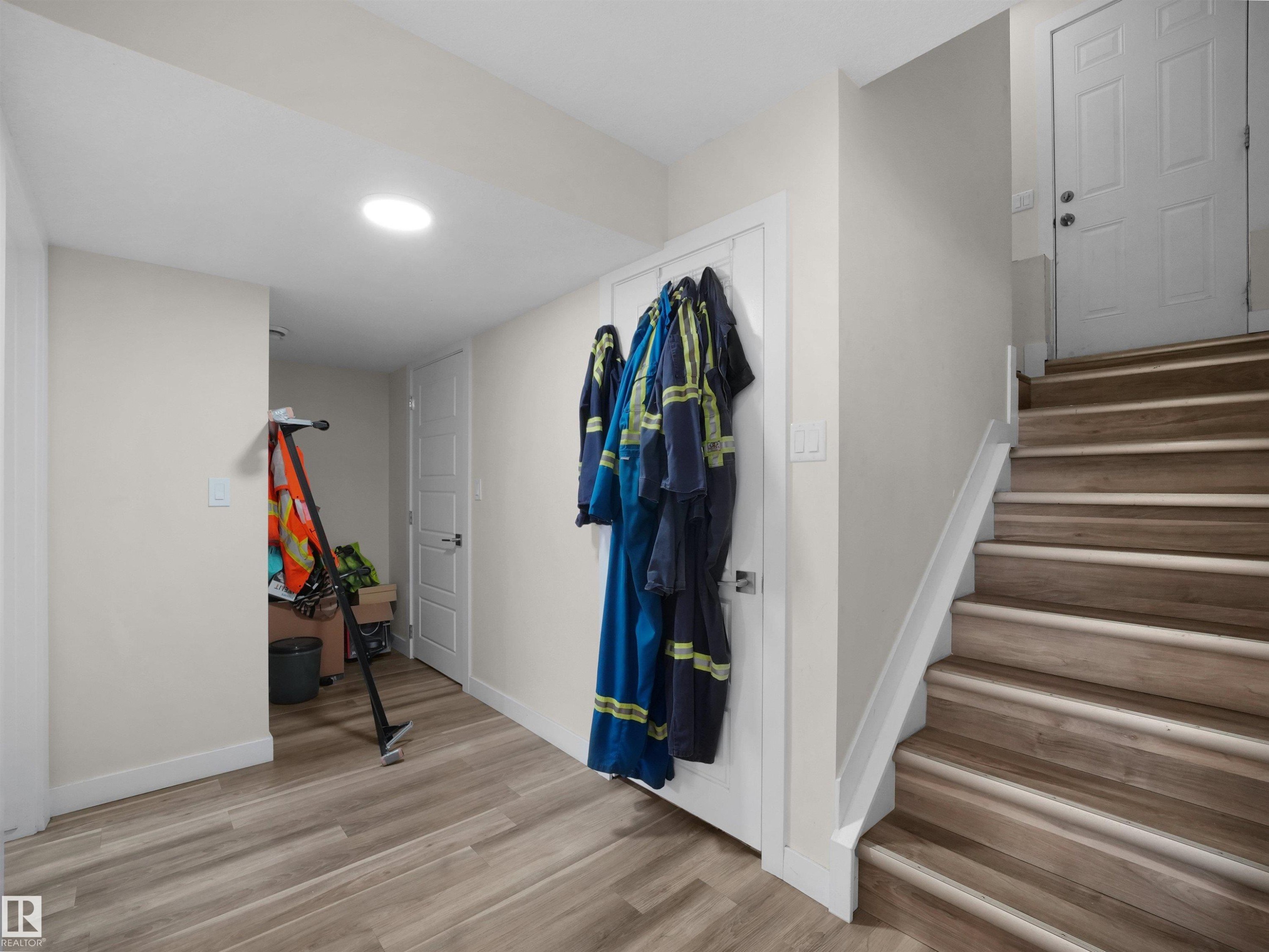 Interior staircase featuring wood-finish treads and risers, white painted stringer, and a white paneled door - 3247 15 Avenue Nw, Edmonton, AB