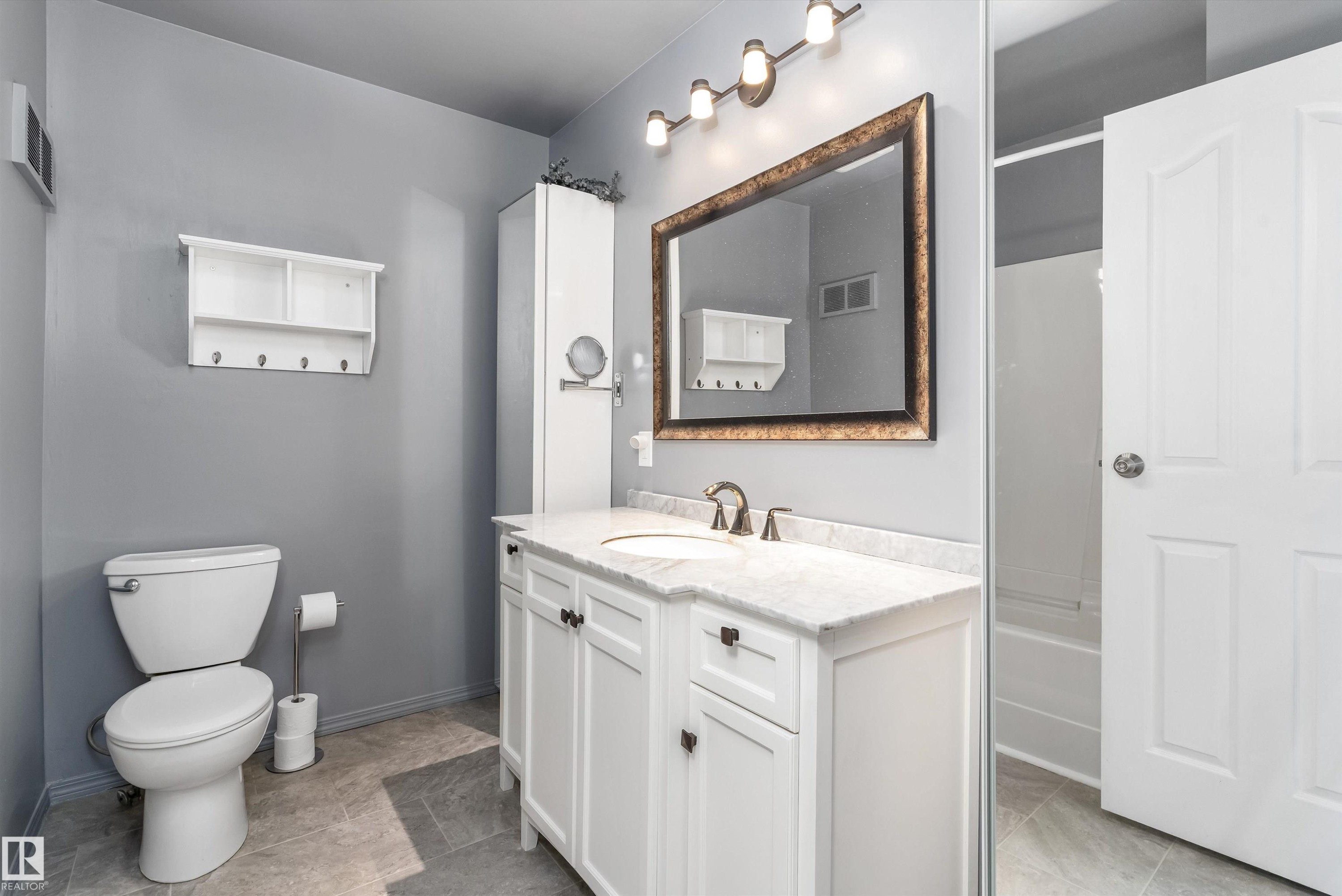 Bathroom featuring a white vanity with a stone-finish countertop, undermount sink, and bronze-finish faucet - 6734 36A Avenue, Edmonton, AB - Indoor Photo Showing Bathroom