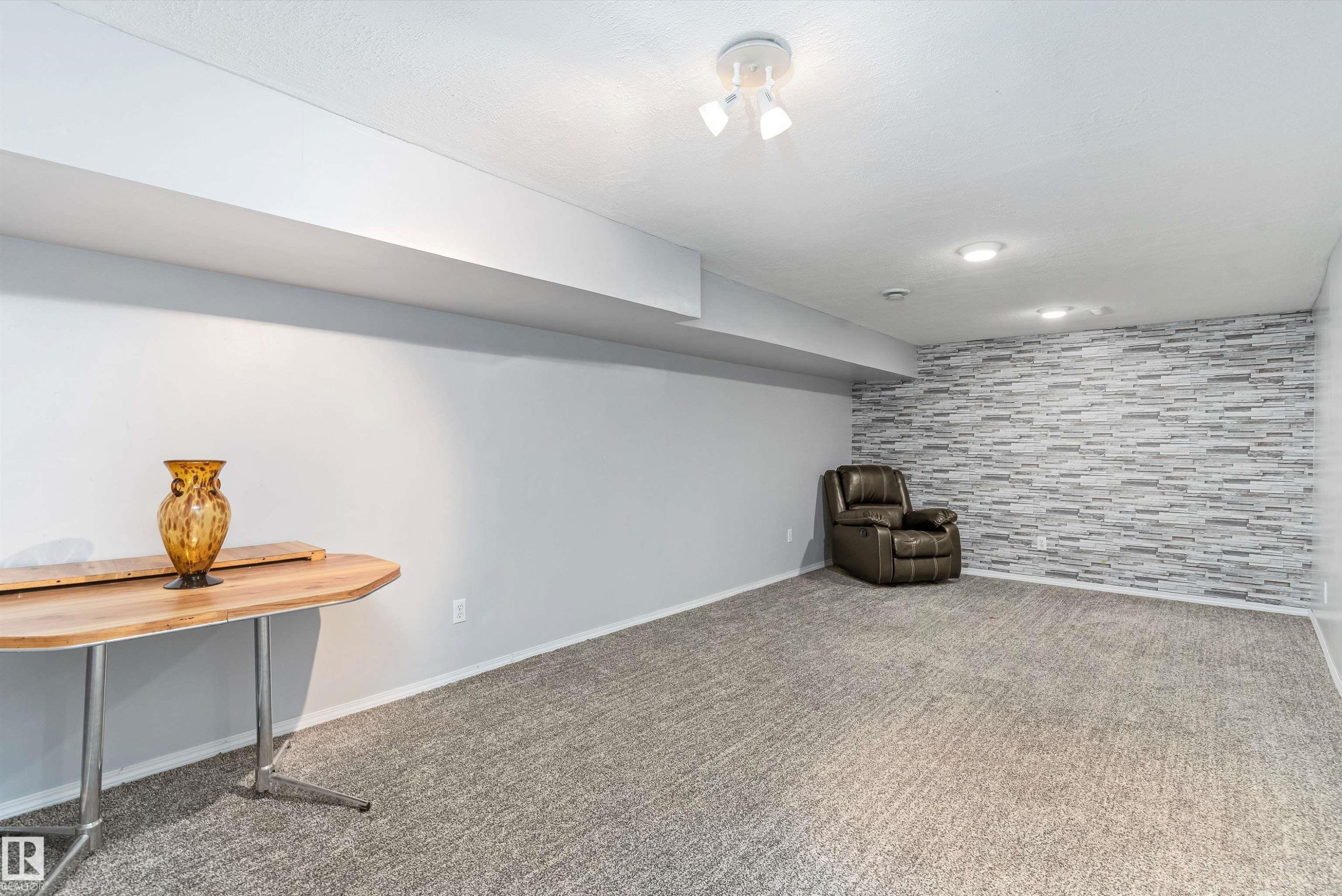 Finished interior space featuring gray textured carpeting, light gray painted walls, and a stone-look accent wall - 6734 36A Avenue, Edmonton, AB - Indoor Photo Showing Other Room