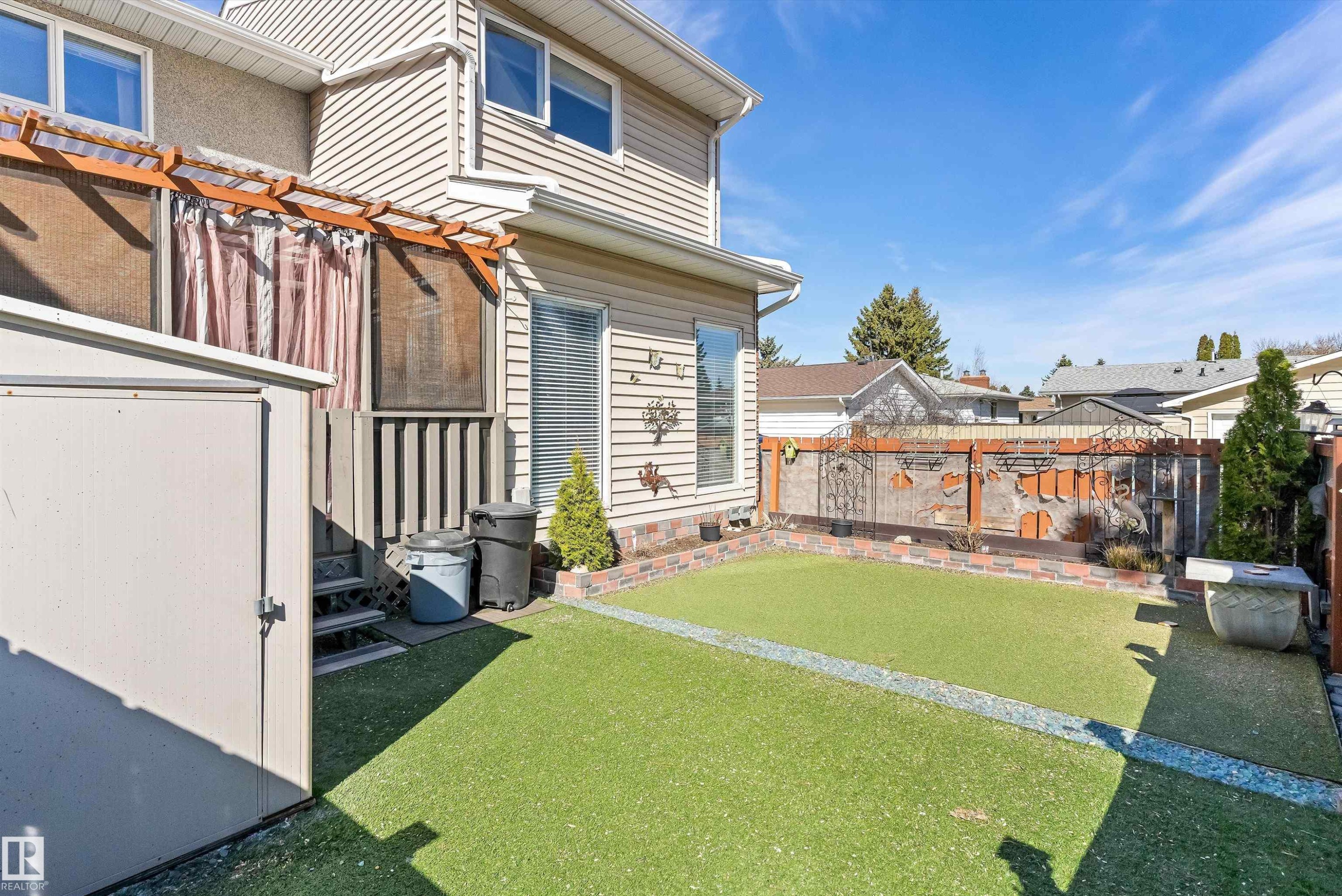 Private rear yard featuring artificial turf, brick-lined planters, and a raised wooden deck with pergola - 6734 36A Avenue, Edmonton, AB - Outdoor