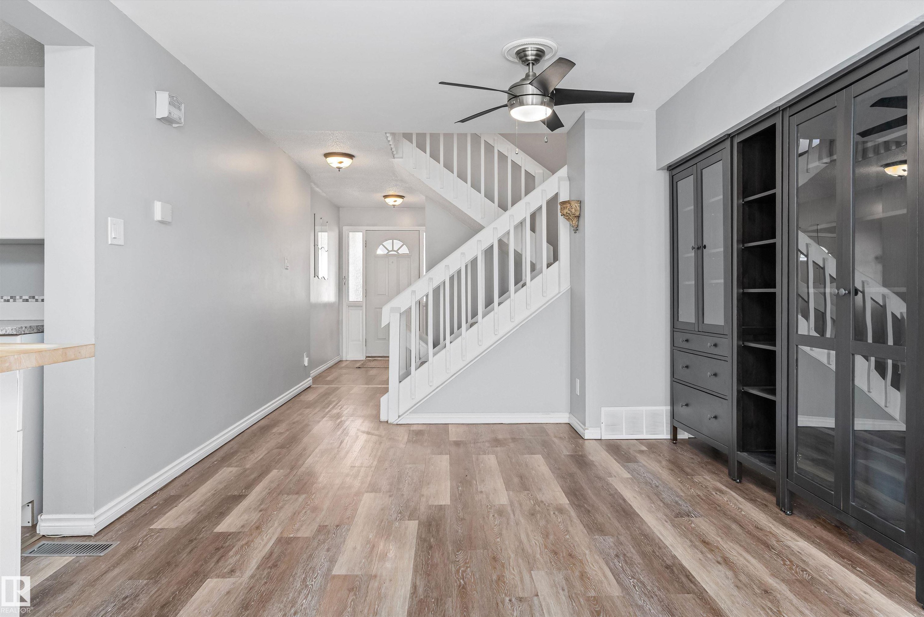 Open-concept living space featuring wood-finish flooring, a contemporary ceiling fan, and a painted staircase with white balusters - 6734 36A Avenue, Edmonton, AB - Indoor Photo Showing Other Room