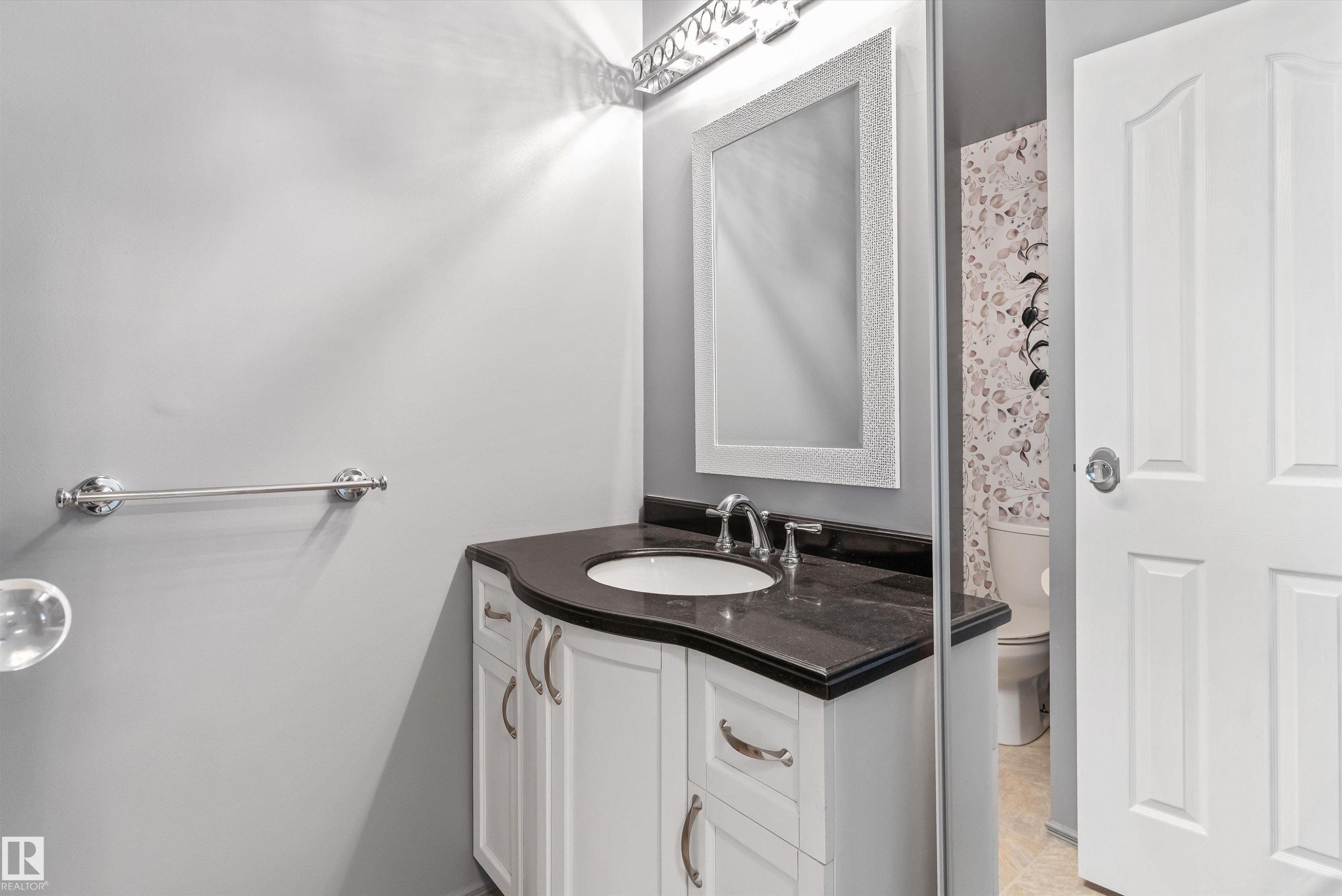 Vanity with integrated sink, dark countertop, and white cabinetry - 6734 36A Avenue, Edmonton, AB - Indoor Photo Showing Bathroom