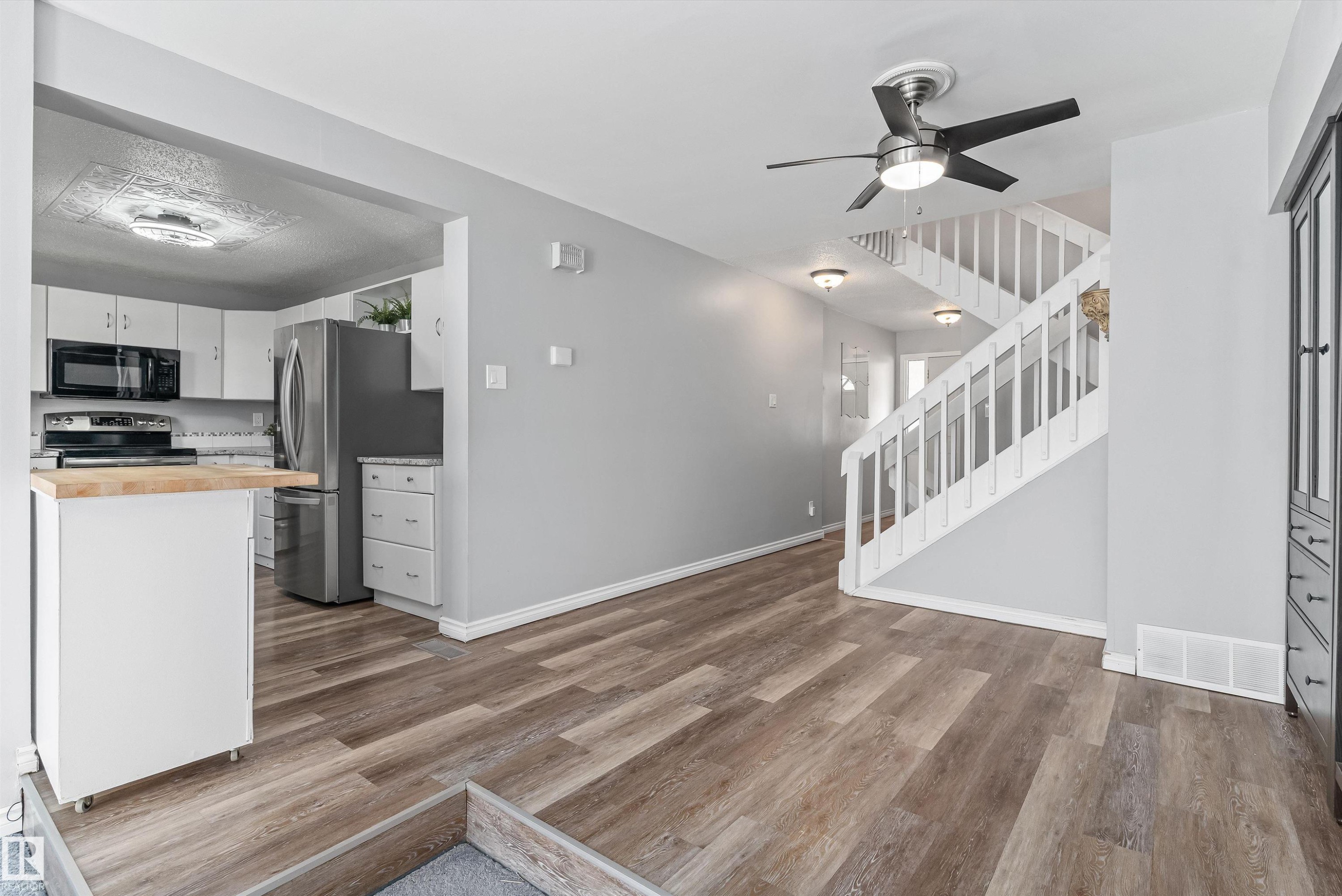 Open concept living area featuring wood-finish flooring, light gray walls, a contemporary ceiling fan, and a white staircase with wood railings - 6734 36A Avenue, Edmonton, AB - Indoor Photo Showing Kitchen