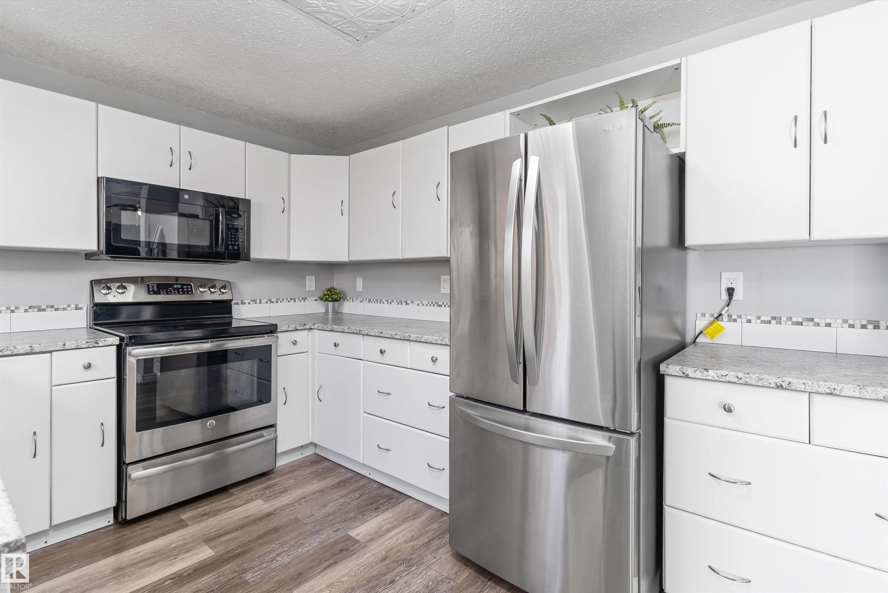 Kitchen featuring white cabinetry, stainless steel appliances, speckled countertops, a mosaic tile backsplash, and wood-finish flooring - 6734 36A Avenue, Edmonton, AB - Indoor Photo Showing Kitchen