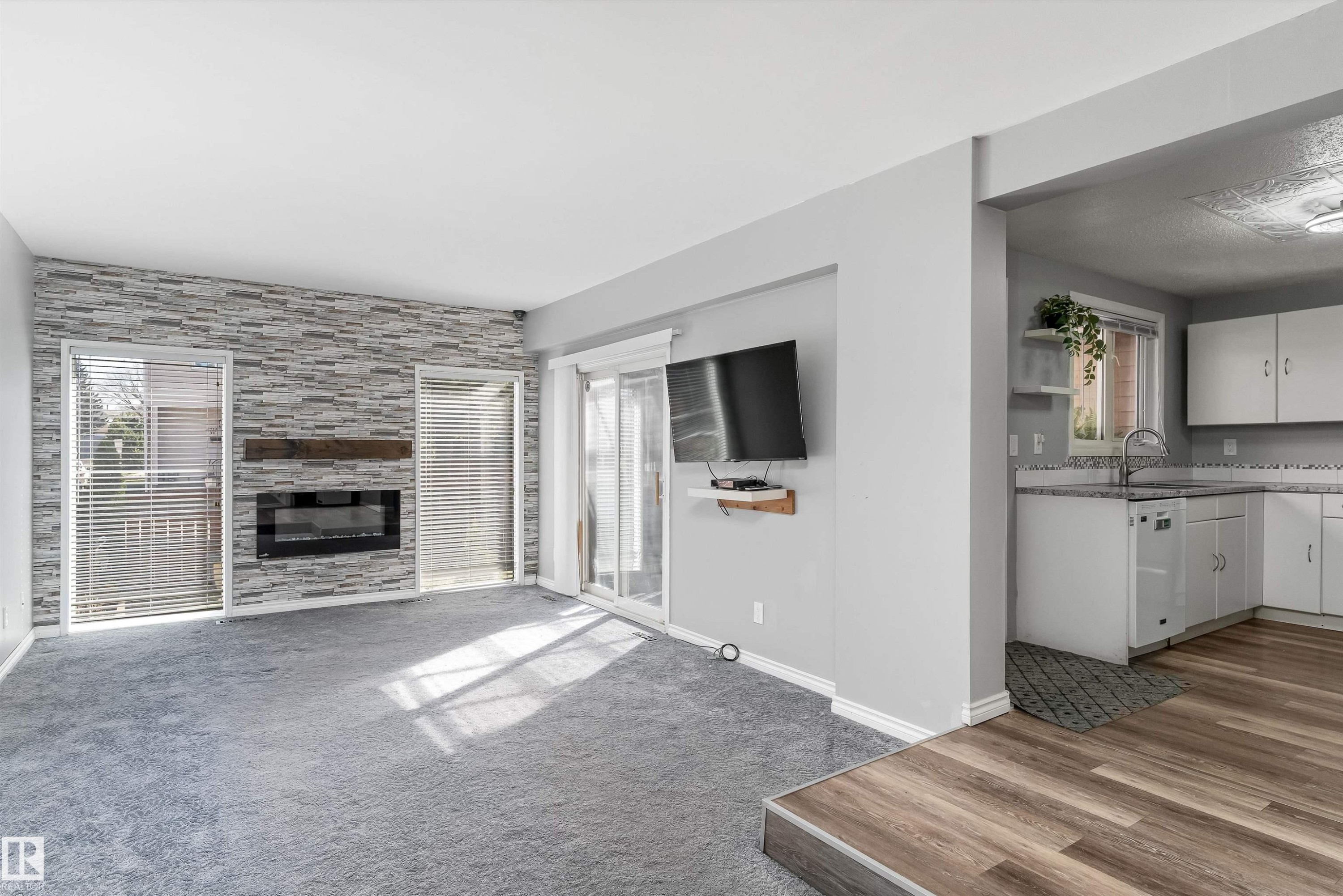 Living area featuring a textured stone-look accent wall with an electric fireplace, a wood mantel, and two vertical windows with blinds - 6734 36A Avenue, Edmonton, AB - Indoor Photo Showing Living Room With Fireplace