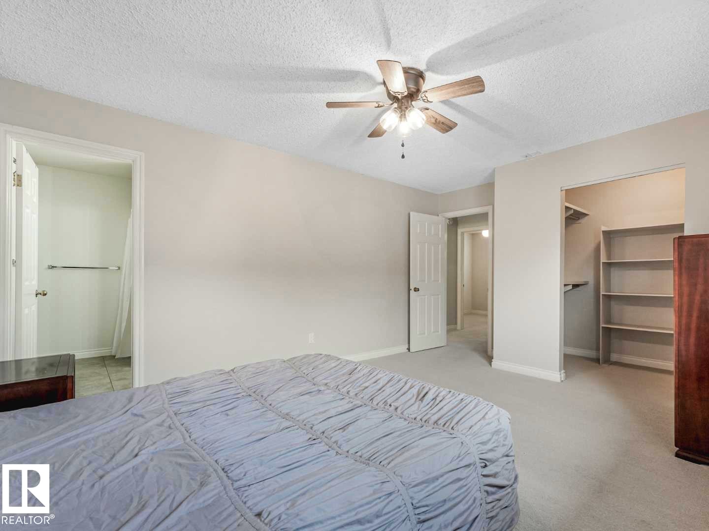 Carpeted bedroom with a ceiling fan, featuring a walk-in closet with built-in shelving, and doorways to additional spaces - 4011 104 Street, Edmonton, AB - Indoor Photo Showing Bedroom