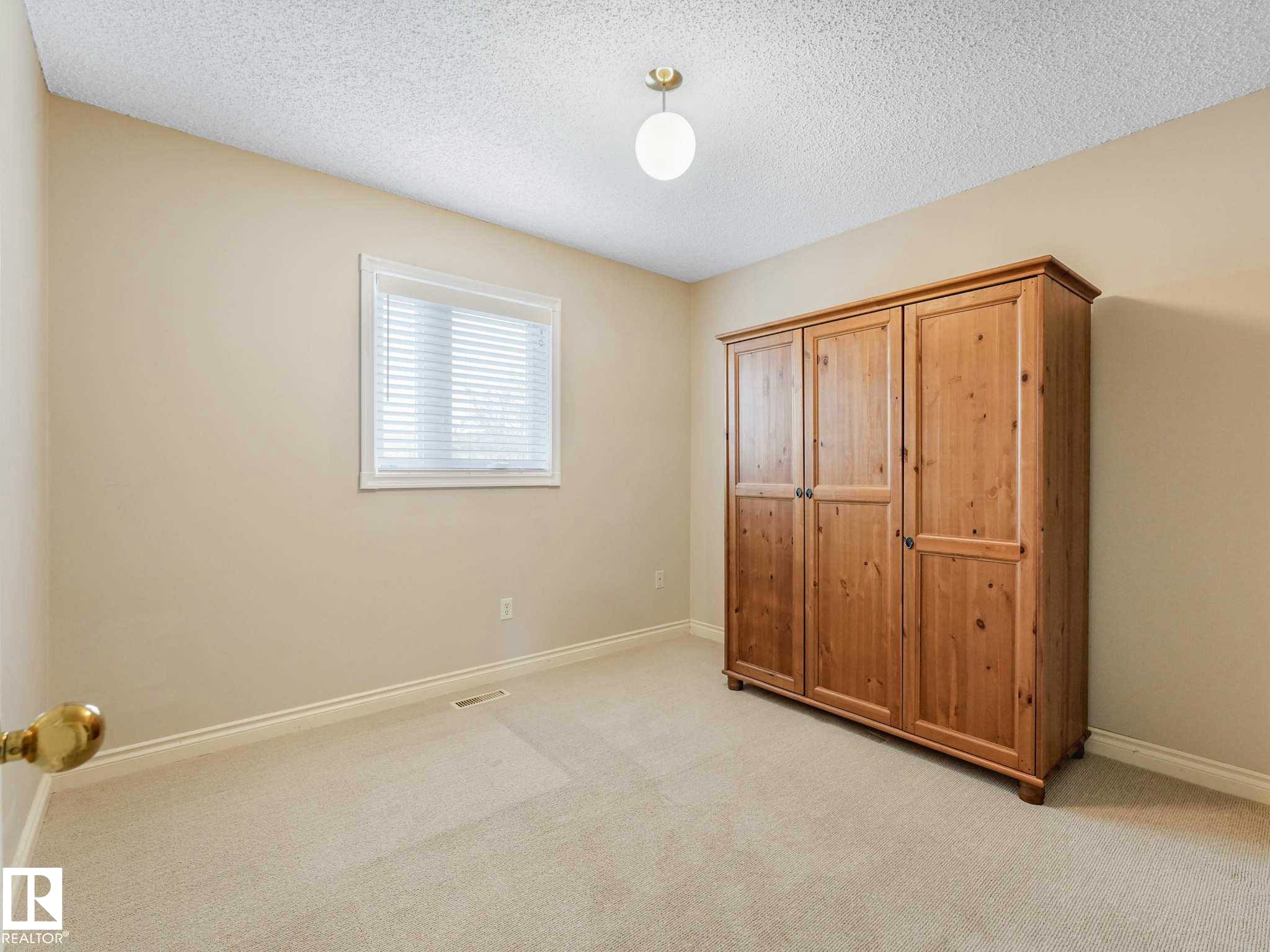 Carpeted room featuring a single window with blinds, a ceiling-mounted light fixture, and neutral-toned walls - 4011 104 Street, Edmonton, AB - Indoor