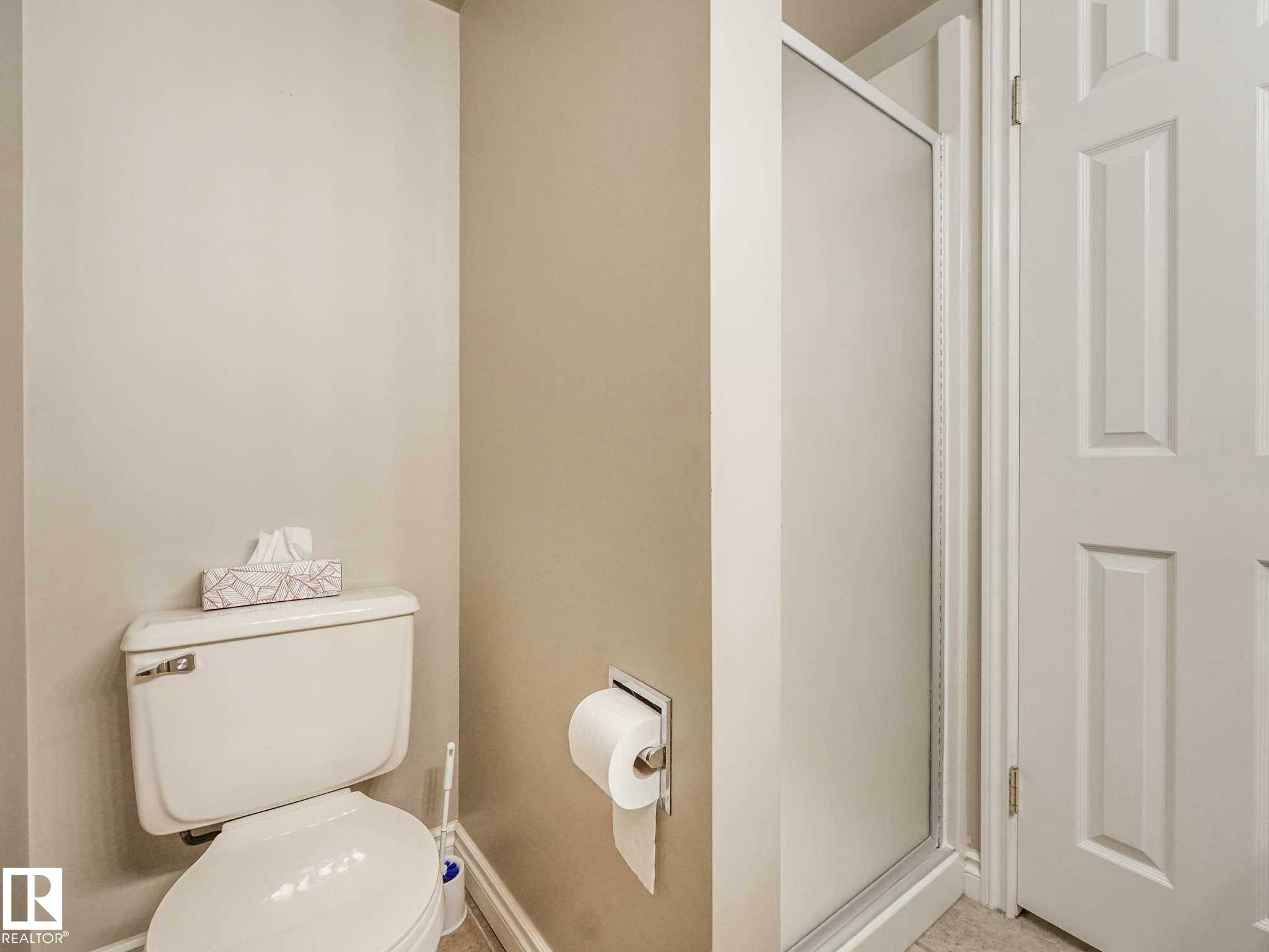 White toilet with a built-in shower stall featuring a frosted glass door and a white paneled door - 4011 104 Street, Edmonton, AB - Indoor Photo Showing Bathroom