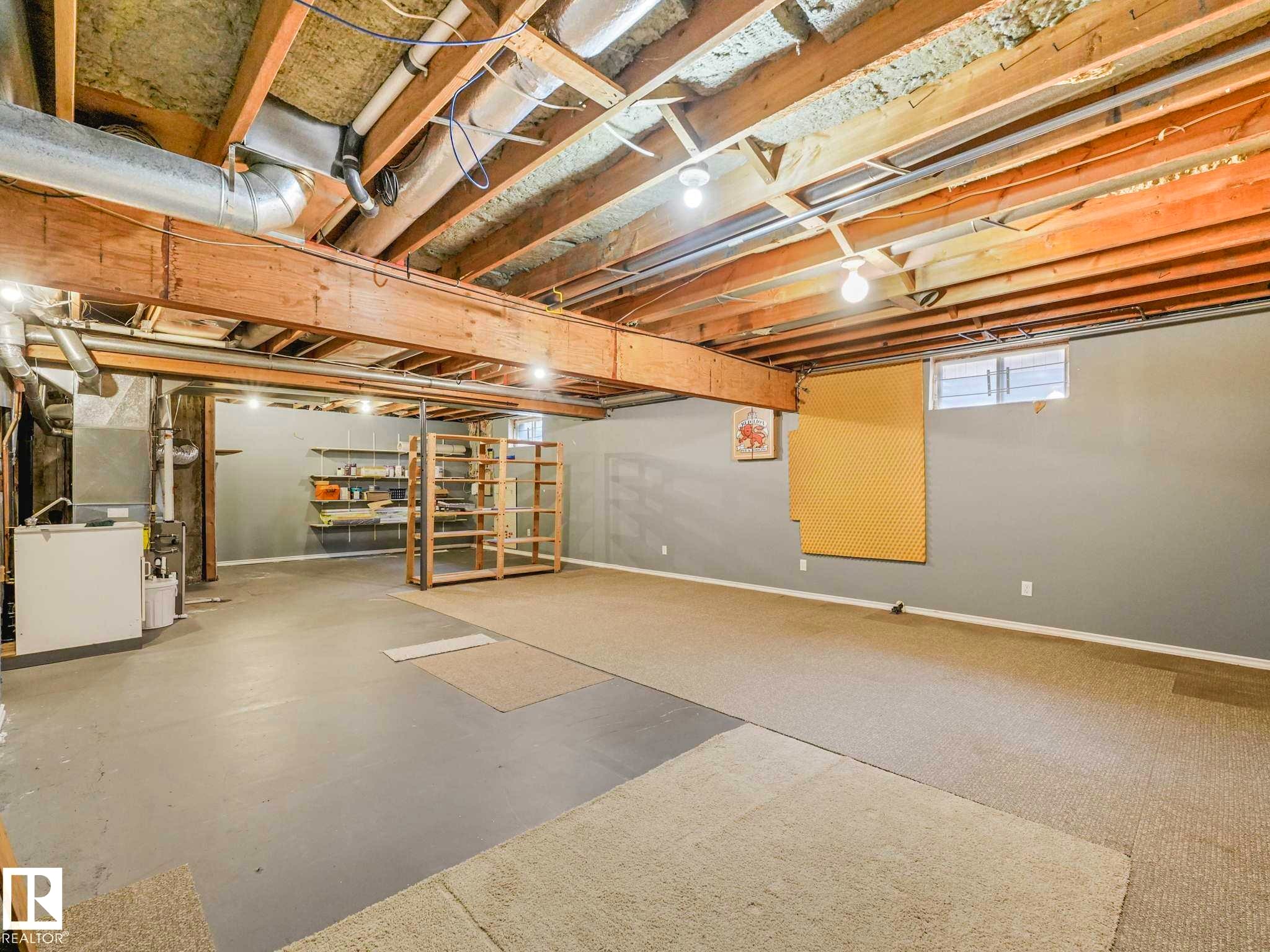 Unfinished basement featuring exposed wood joists and structural beams, painted concrete flooring, and existing utility connections - 4011 104 Street, Edmonton, AB - Indoor Photo Showing Basement