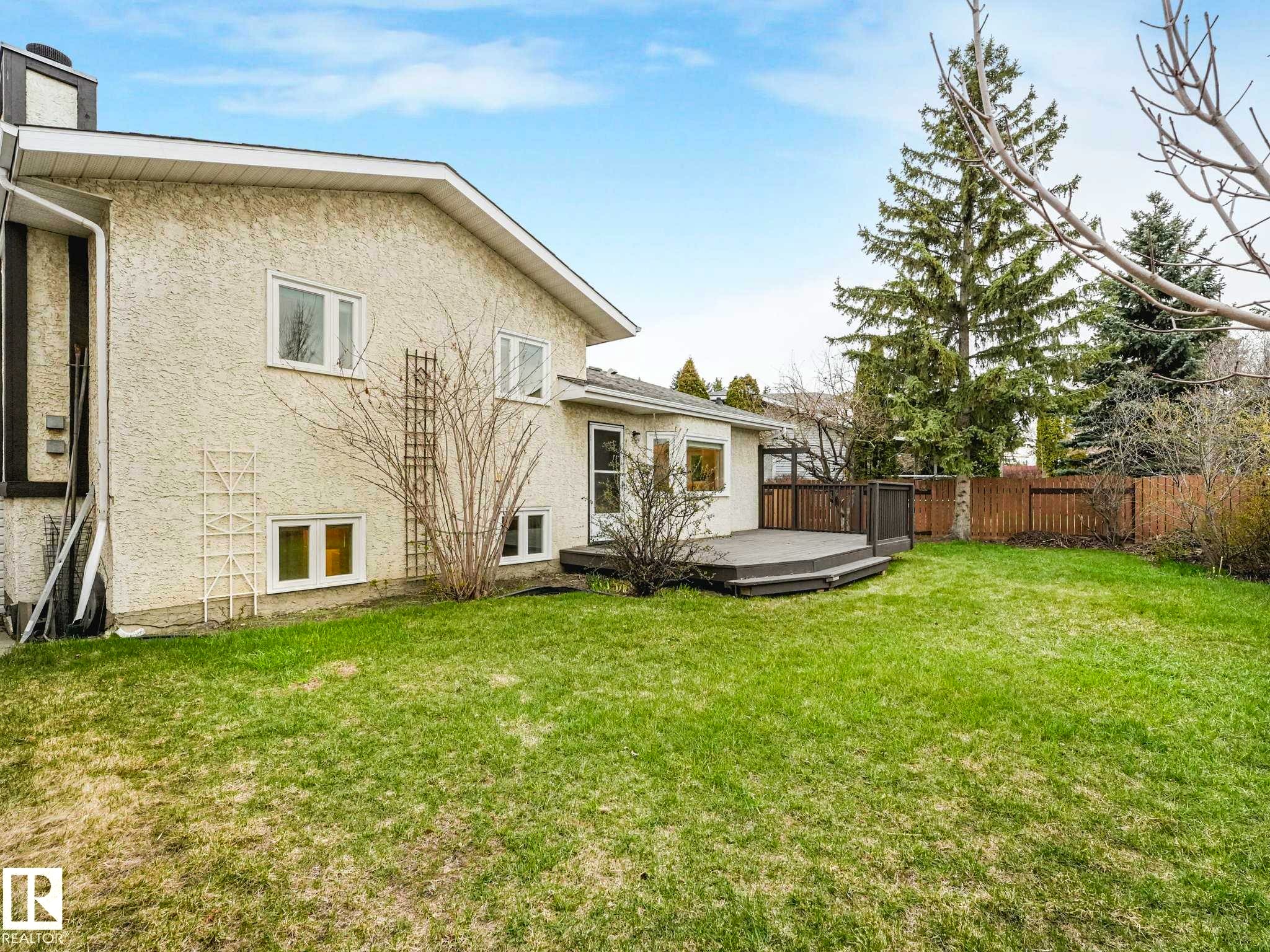 Rear exterior featuring stucco siding, multiple windows, and a multi-level deck with dark composite decking - 4011 104 Street, Edmonton, AB - Outdoor