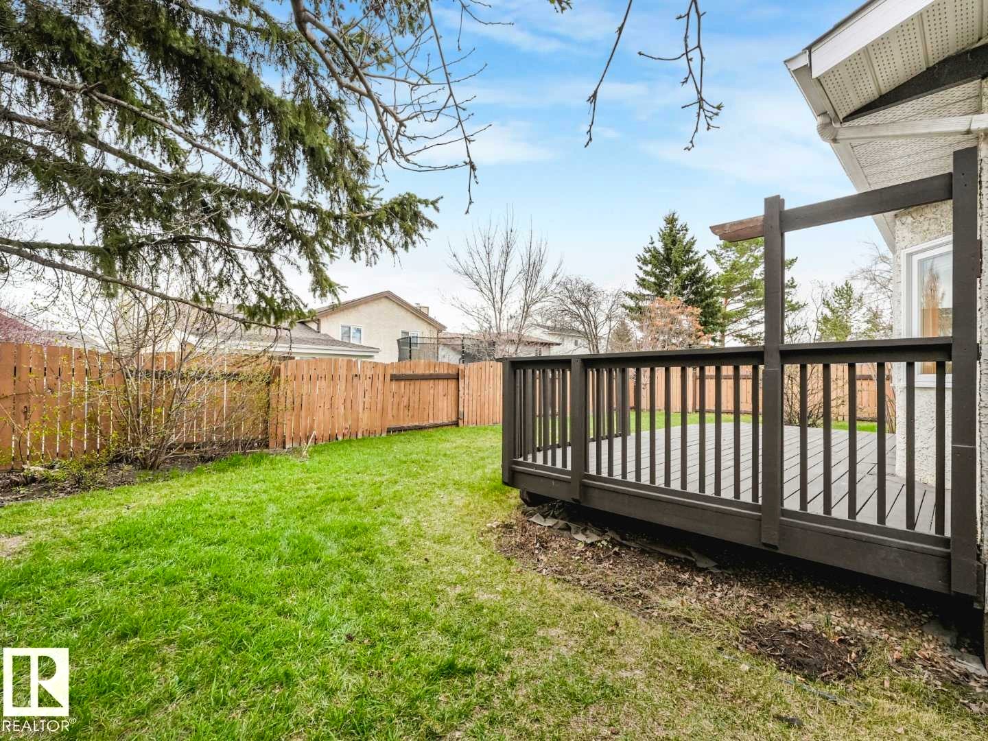 Private backyard featuring a wooden privacy fence, a spacious deck with dark grey railings, and an expansive lawn area - 4011 104 Street, Edmonton, AB - Outdoor