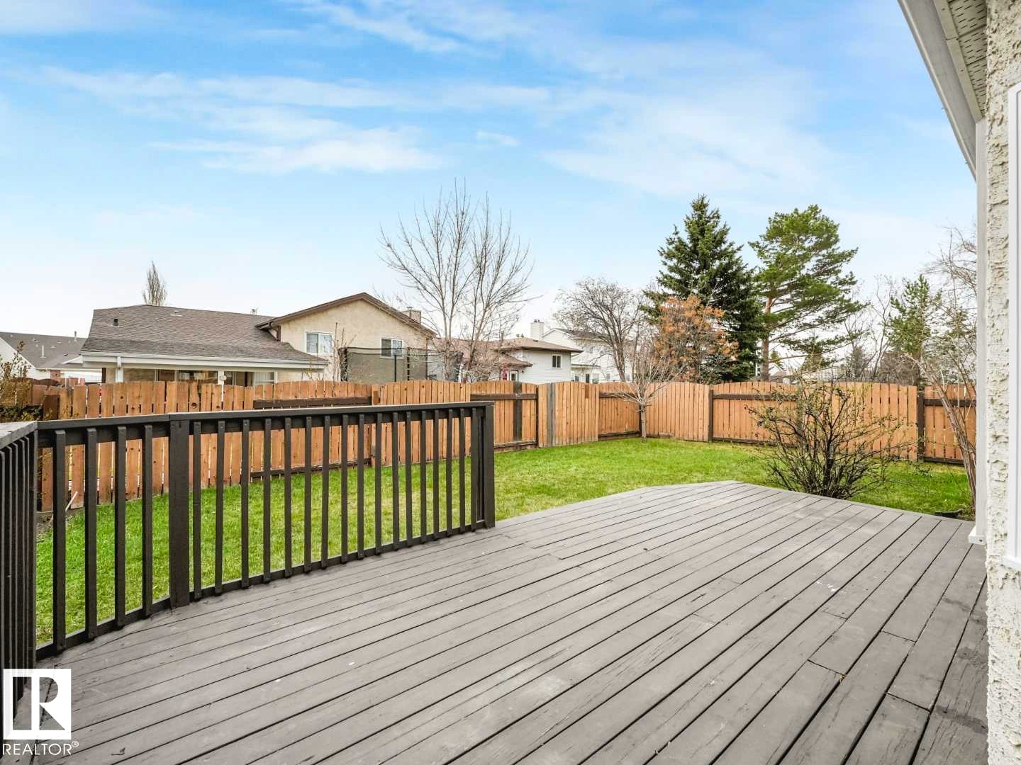 Spacious outdoor deck with dark wood-finish planking and railing, overlooking a fenced backyard with green lawn - 4011 104 Street, Edmonton, AB - Outdoor With Deck Patio Veranda
