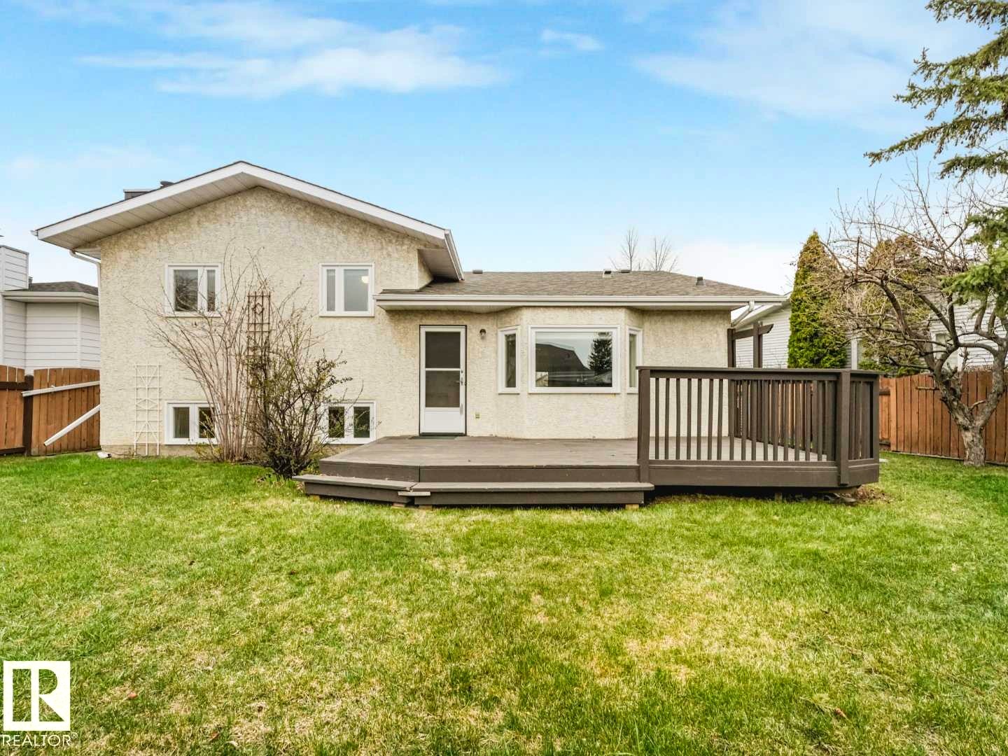 Spacious backyard featuring a large composite deck with railing, a grass lawn, and a light-colored stucco exterior - 4011 104 Street, Edmonton, AB - Outdoor With Deck Patio Veranda