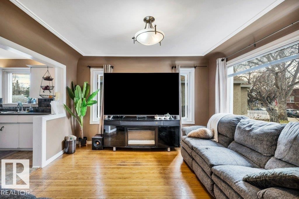 Living area featuring wood-finish flooring, a large front-facing window, and a built-in media console - 11445 68 Street, Edmonton, AB - Indoor Photo Showing Living Room