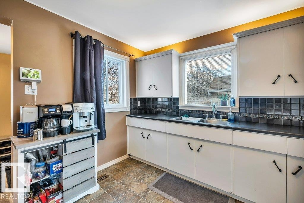 Kitchen featuring white cabinetry with dark hardware, dark countertops, and a dark square tile backsplash - 11445 68 Street, Edmonton, AB - Indoor Photo Showing Kitchen