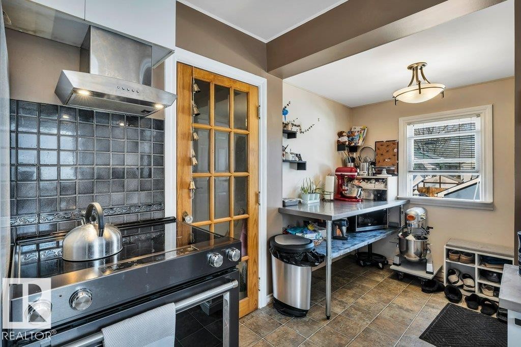 Kitchen area featuring a stainless steel range hood, black tile backsplash, and a paneled wood door - 11445 68 Street, Edmonton, AB - Indoor Photo Showing Kitchen