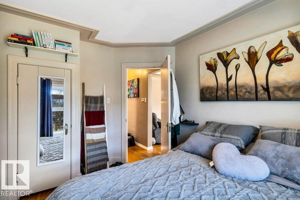 Interior room featuring crown molding, a built-in wall shelf, a door with an attached full-length mirror, and wood-finish flooring - 11445 68 Street, Edmonton, AB - Indoor Photo Showing Bedroom