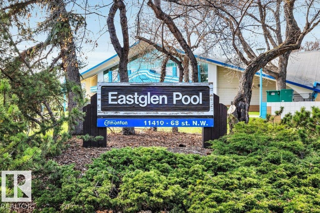 Community sign for Eastglen Pool, featuring a building with blue trim, surrounded by mature trees and manicured shrubbery - 11445 68 Street, Edmonton, AB - Outdoor