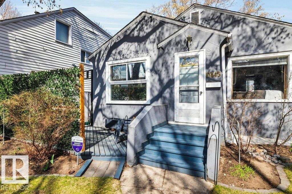 Gray stucco exterior featuring white trim, a front porch with blue-painted steps, and a white storm door - 11445 68 Street, Edmonton, AB - Outdoor