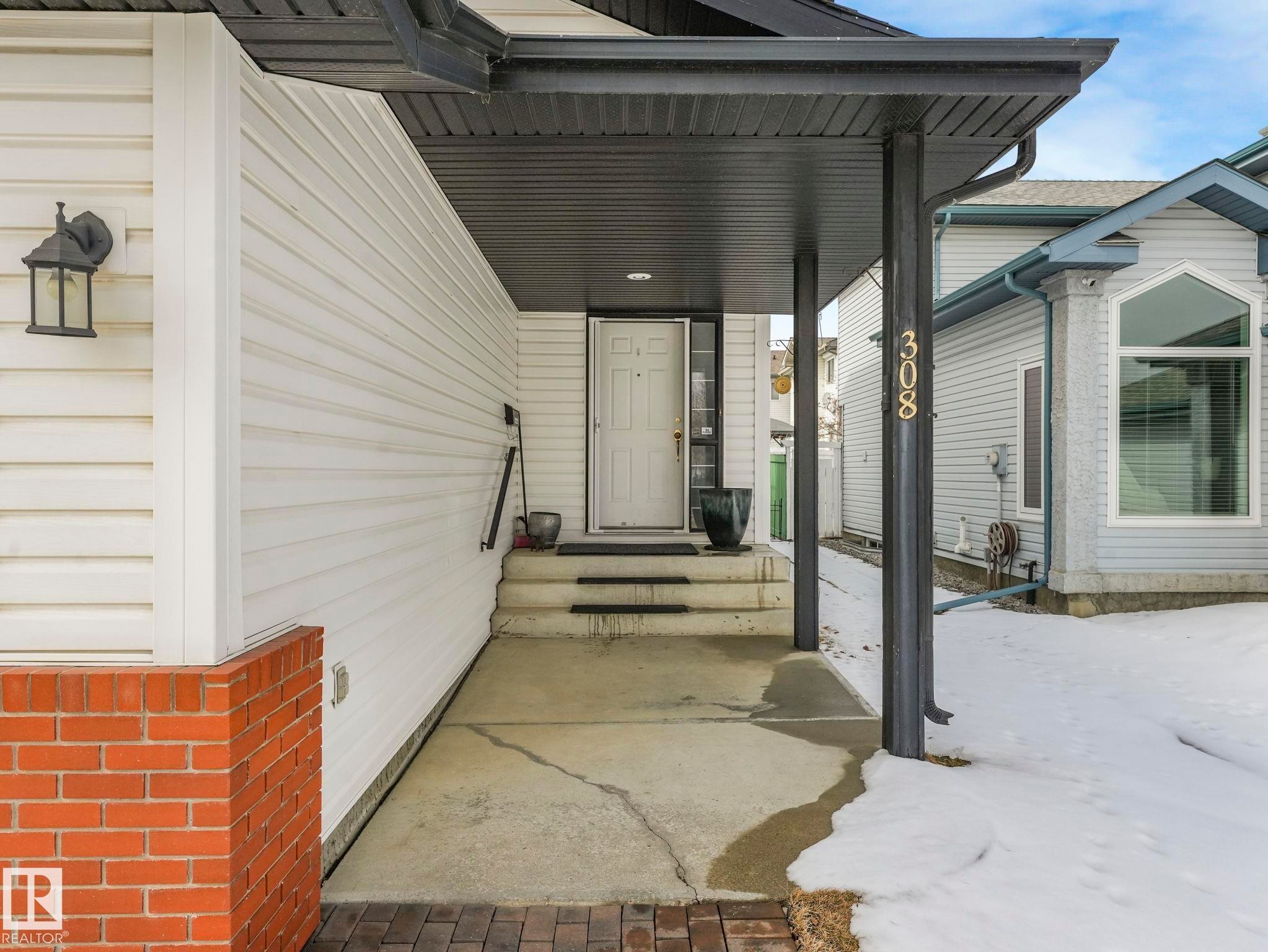 The property features a covered front entrance with a white door, brick detailing, and white siding - 308 Beringer Crescent, Edmonton, AB - Outdoor With Exterior