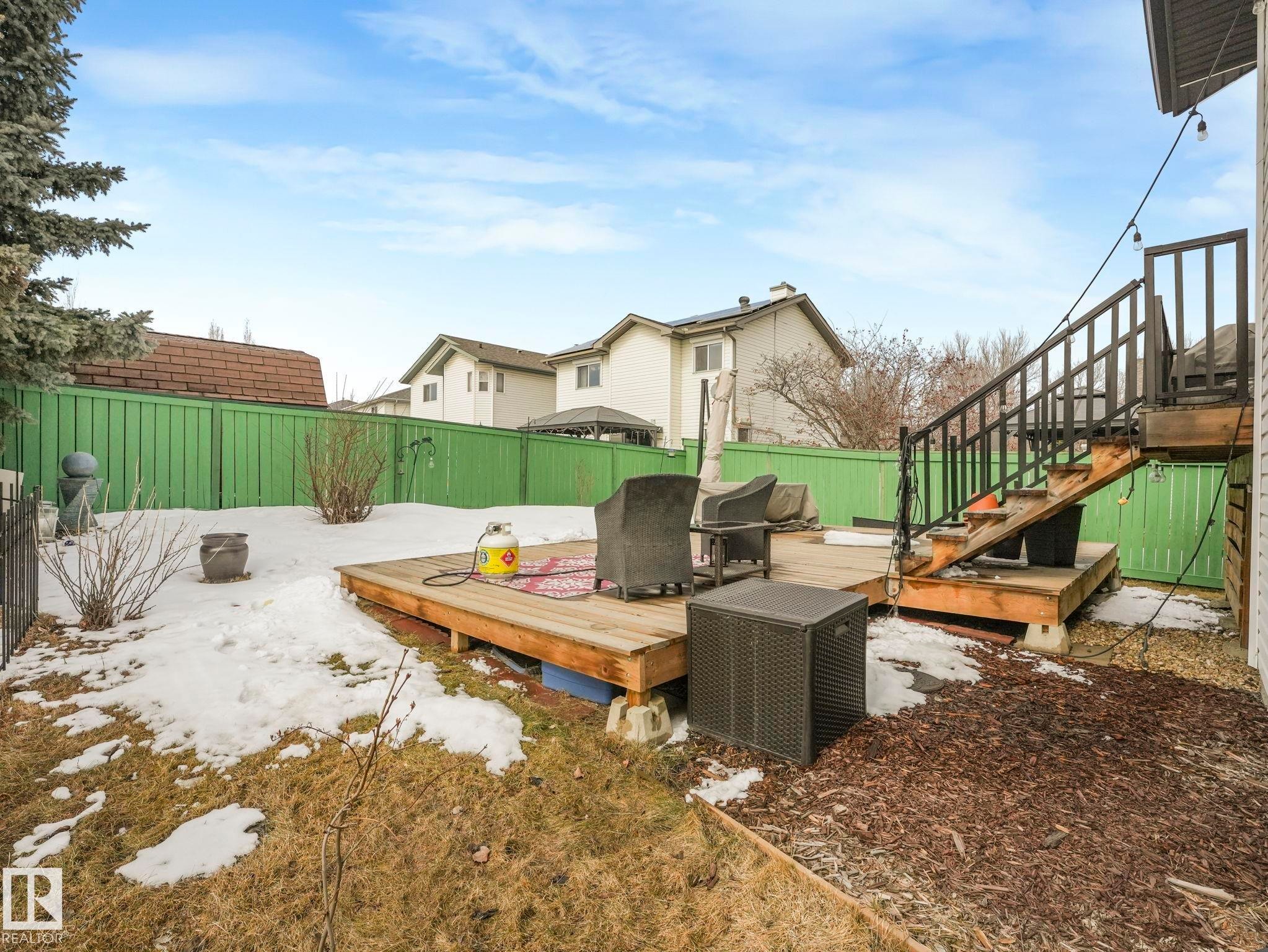 The property features an extensive outdoor deck with stairs, surrounded by a green fence and mature trees - 308 Beringer Crescent, Edmonton, AB - Outdoor With Deck Patio Veranda