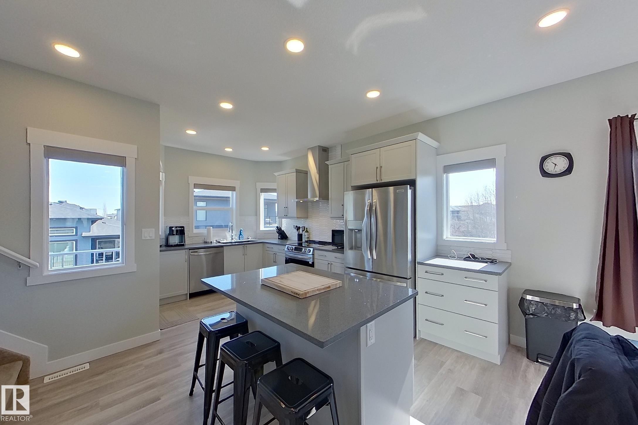 Open-concept kitchen featuring light-toned cabinetry, stainless steel appliances, a center island with seating, recessed lighting, and wood-finish flooring - 33 150 Everitt Dr, St. Albert, AB - Indoor Photo Showing Kitchen