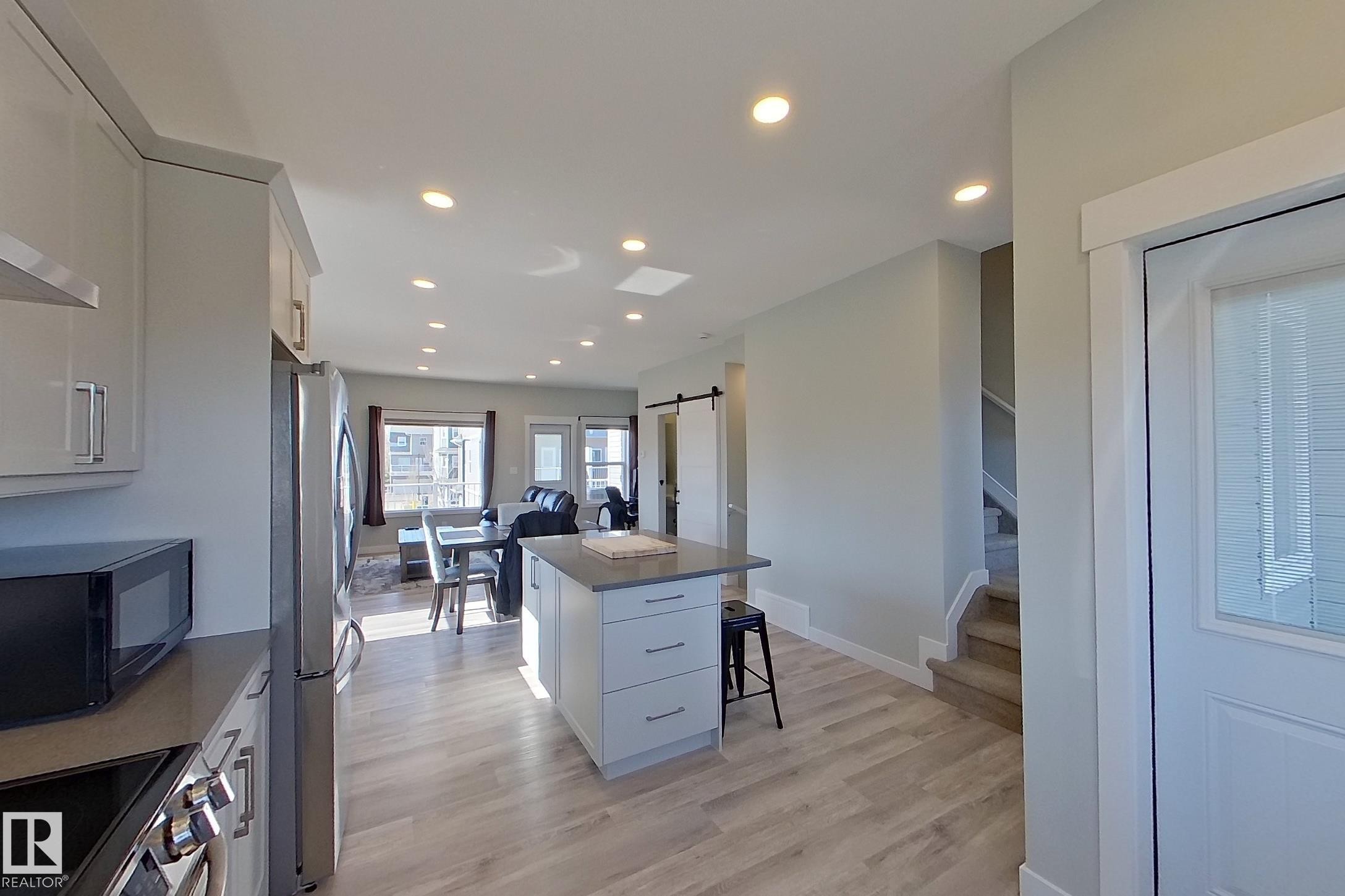 Modern kitchen featuring an island with a stone countertop, stainless steel appliances, recessed lighting, and wood-finish flooring - 33 150 Everitt Dr, St. Albert, AB - Indoor Photo Showing Kitchen