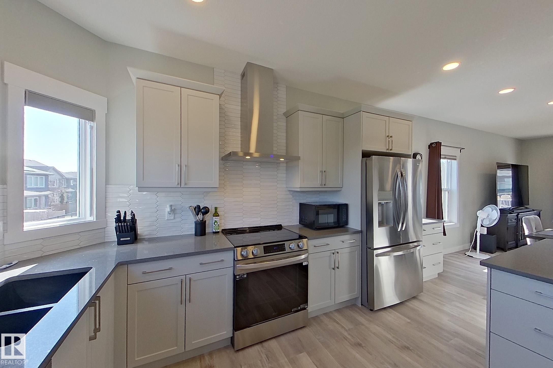 Modern kitchen featuring light cabinetry, stainless steel appliances, a white tile backsplash, and light wood-finish flooring - 33 150 Everitt Dr, St. Albert, AB - Indoor Photo Showing Kitchen With Double Sink