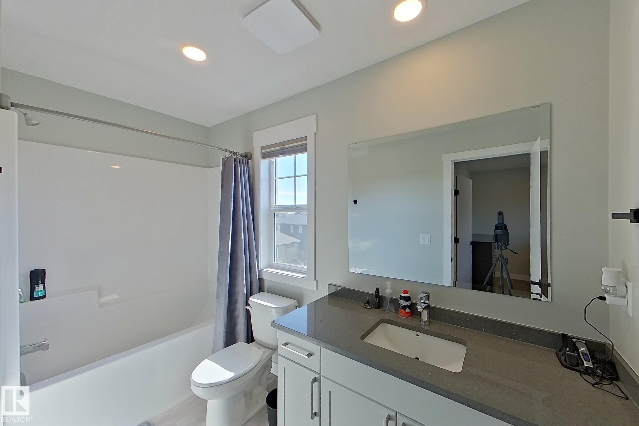 Bathroom featuring a single vanity with an integrated sink, a rectangular mirror, and a full-size bathtub with a shower - 33 150 Everitt Dr, St. Albert, AB - Indoor Photo Showing Bathroom