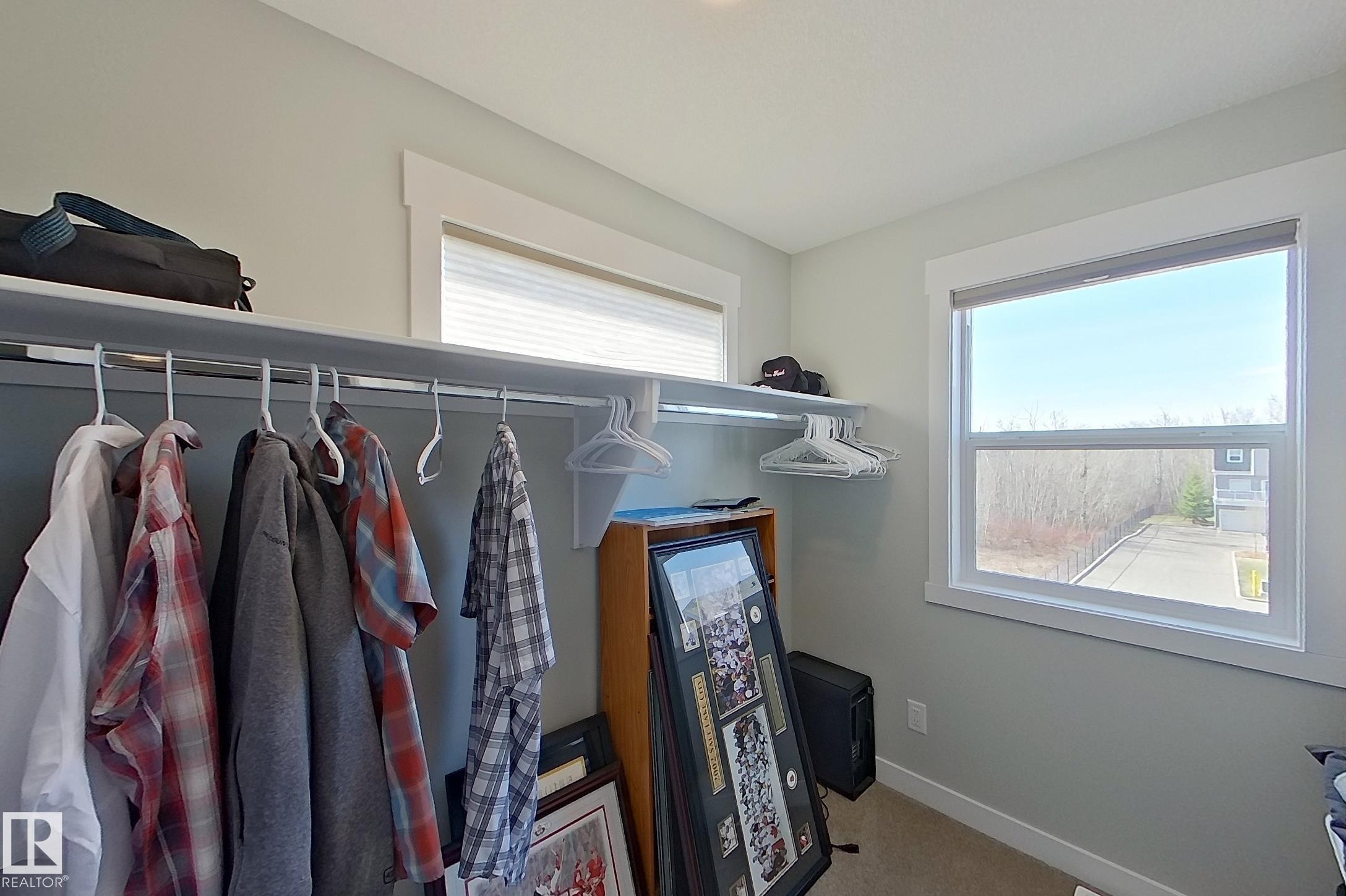 Well-lit interior space featuring dual windows with blinds, light gray walls, white trim, and a built-in closet system with shelving and hanging rods - 33 150 Everitt Dr, St. Albert, AB - Indoor With Storage