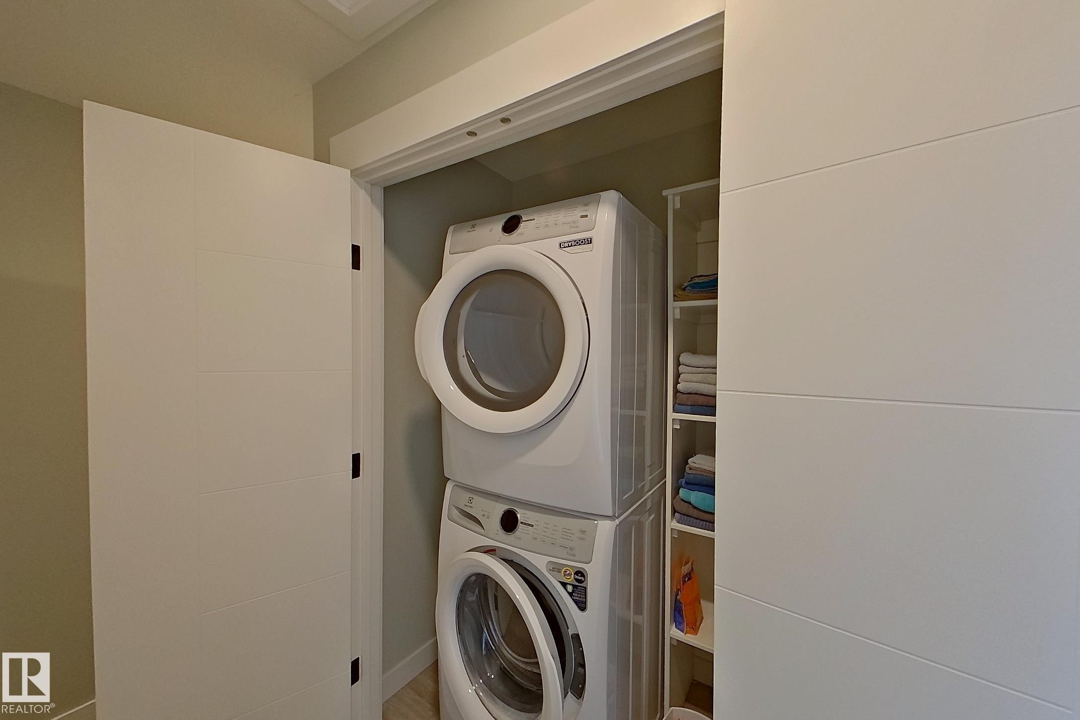 Dedicated laundry closet featuring a stacked washer and dryer, integrated shelving, white shaker-style doors, and light-toned wall paint - 33 150 Everitt Dr, St. Albert, AB - Indoor Photo Showing Laundry Room