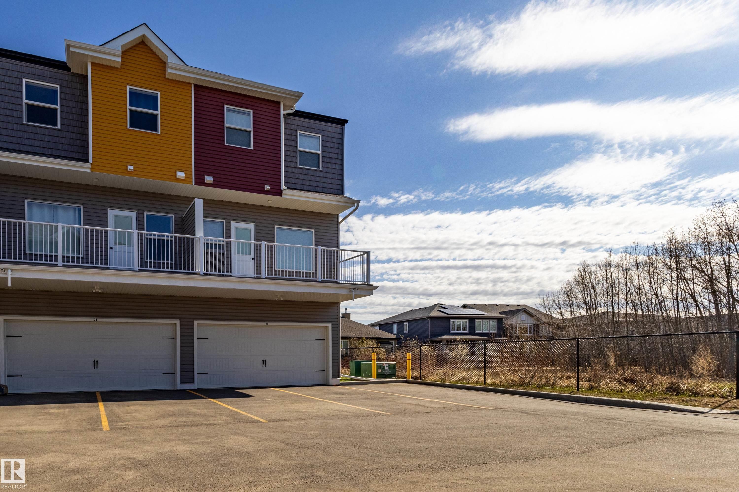 Multi-level exterior with varied siding, private balconies, and integrated garages, complemented by an asphalt parking area - 33 150 Everitt Dr, St. Albert, AB - Outdoor