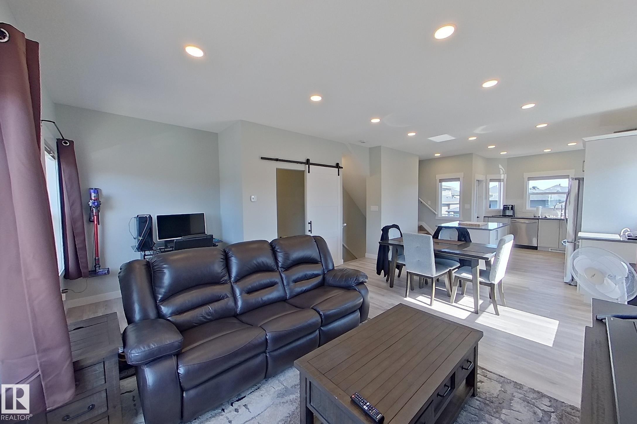 Open-concept living area featuring light-toned wood-finish flooring, recessed lighting, and a modern barn door - 33 150 Everitt Dr, St. Albert, AB - Indoor Photo Showing Living Room