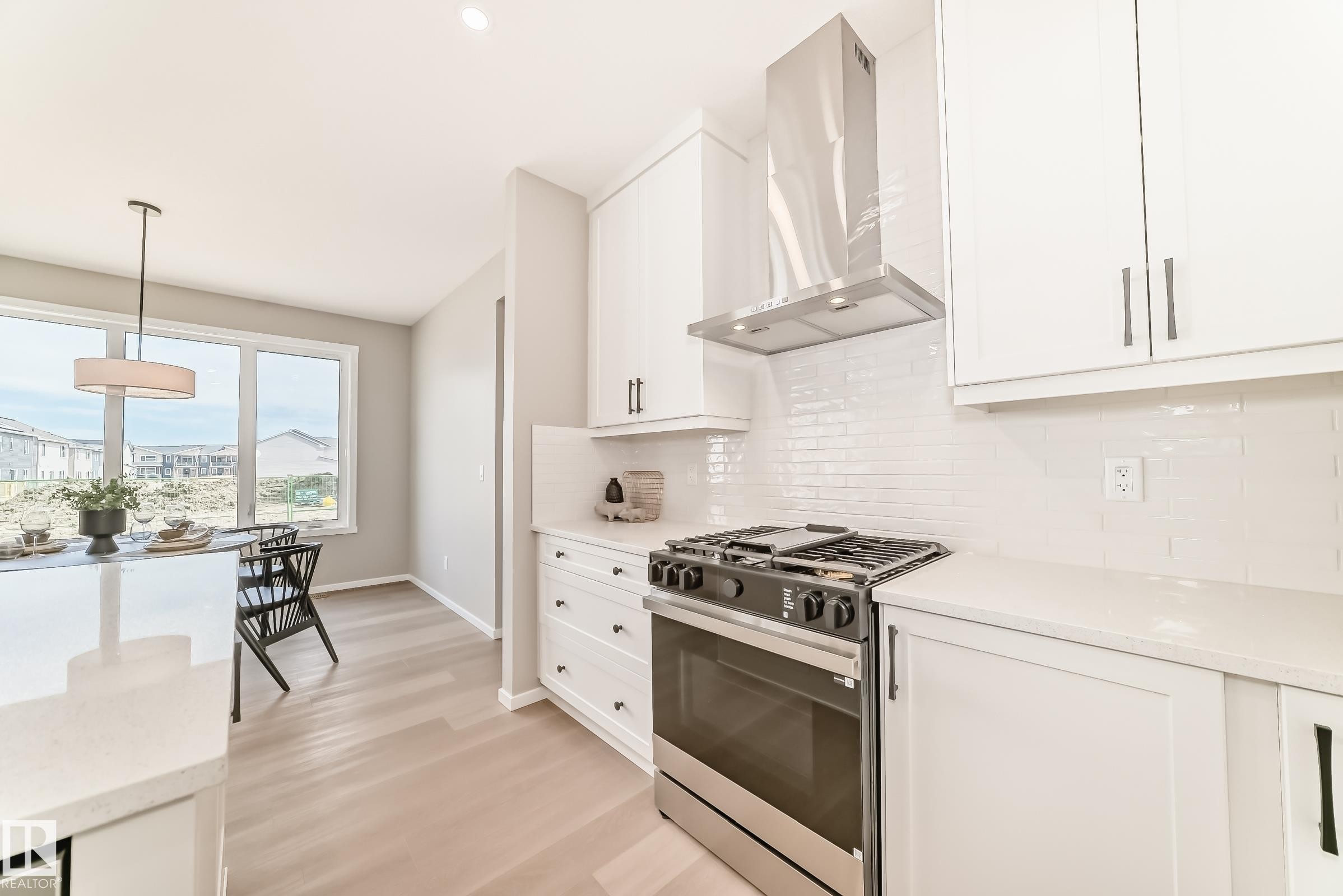 Modern kitchen featuring white cabinetry, stainless steel range with overhead vent hood, white subway tile backsplash, and light wood-finish flooring - 1603 206 Street, Edmonton, AB - Indoor Photo Showing Kitchen With Upgraded Kitchen