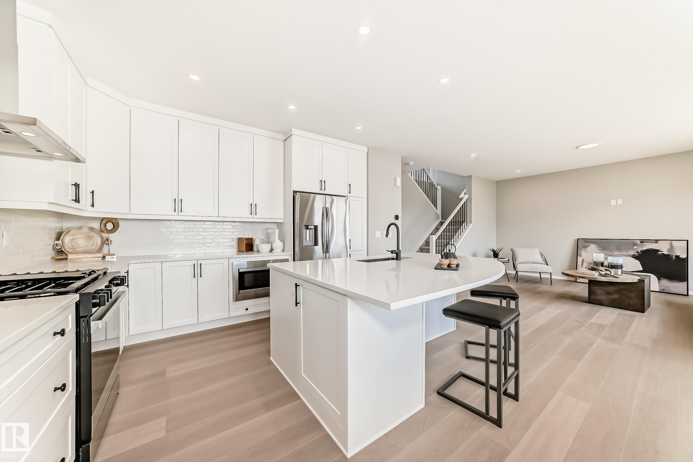 Modern kitchen featuring a white curved island with seating, white shaker-style cabinetry, and stainless steel appliances - 1603 206 Street, Edmonton, AB - Indoor Photo Showing Kitchen With Stainless Steel Kitchen With Upgraded Kitchen