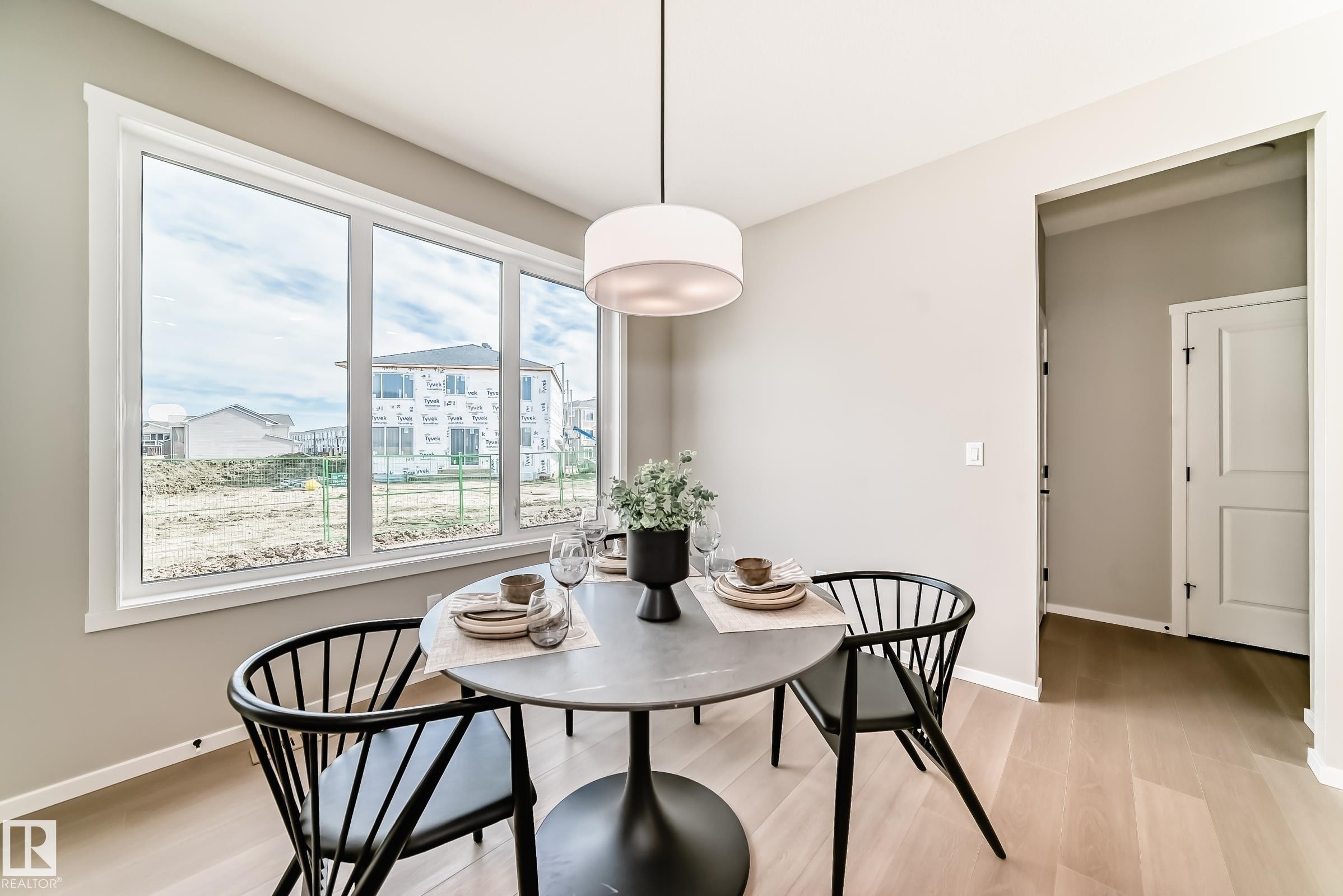 Bright dining area featuring a large picture window, a modern drum pendant light fixture, light wood-finish flooring, and neutral wall tones - 1603 206 Street, Edmonton, AB - Indoor Photo Showing Dining Room