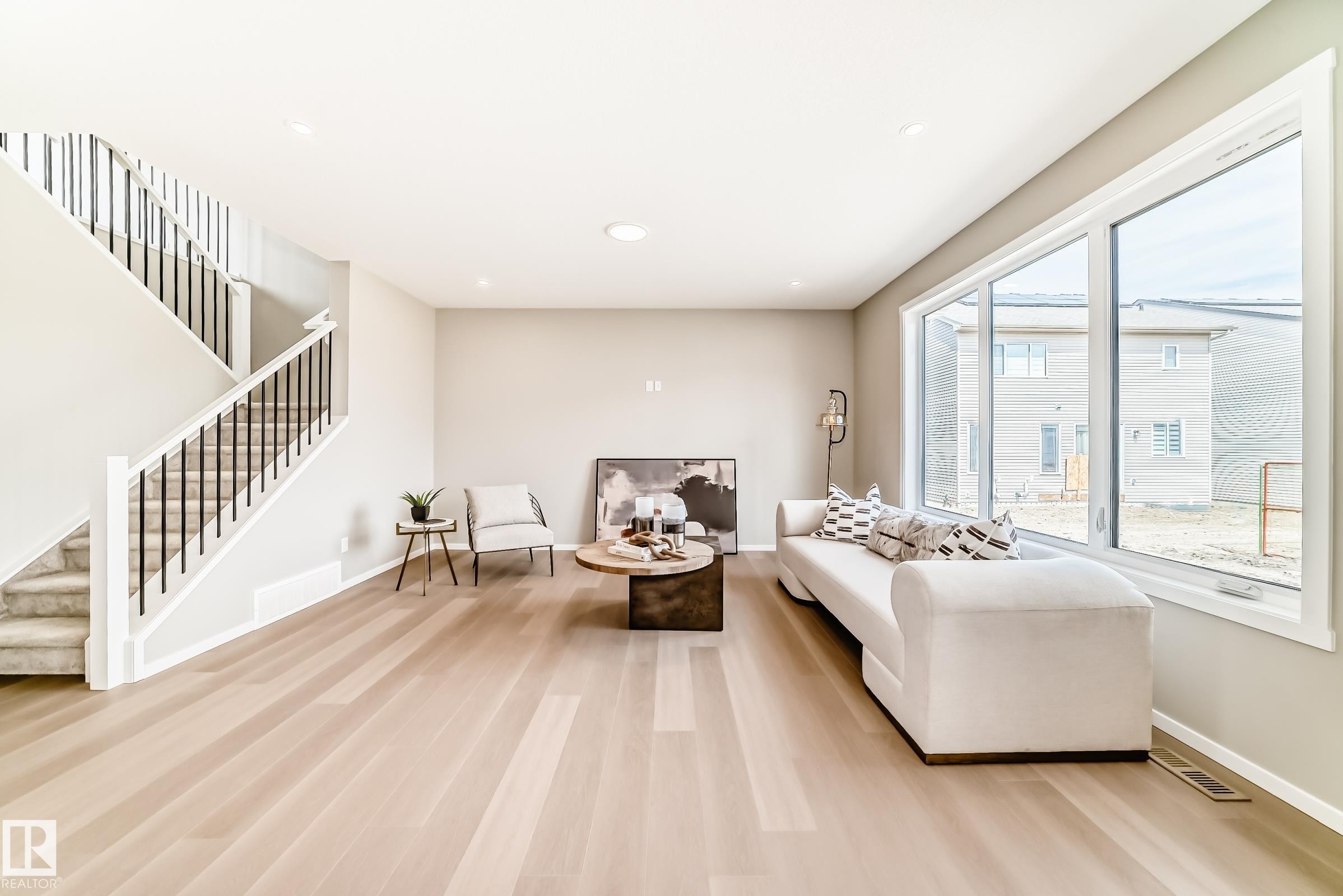 Open-concept living space featuring wood-finish flooring, a contemporary staircase with black spindles, large windows providing natural illumination, and recessed ceiling lighting - 1603 206 Street, Edmonton, AB - Indoor Photo Showing Other Room