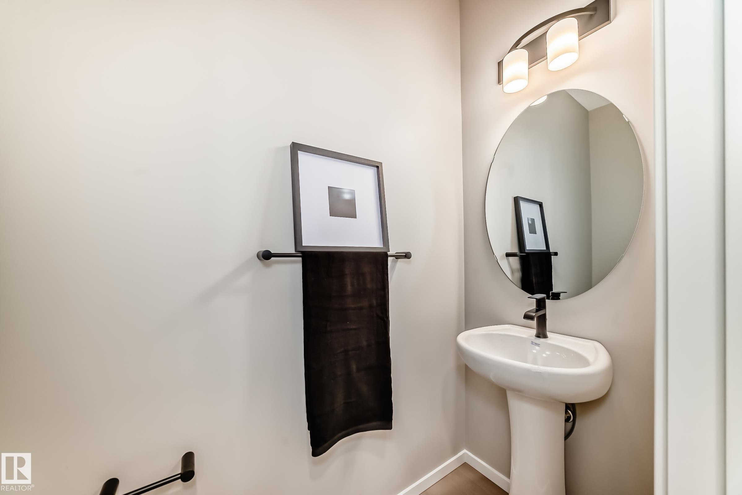 Pedestal sink with matte black faucet, round mirror, and modern wall-mounted light fixture - 1603 206 Street, Edmonton, AB - Indoor Photo Showing Bathroom