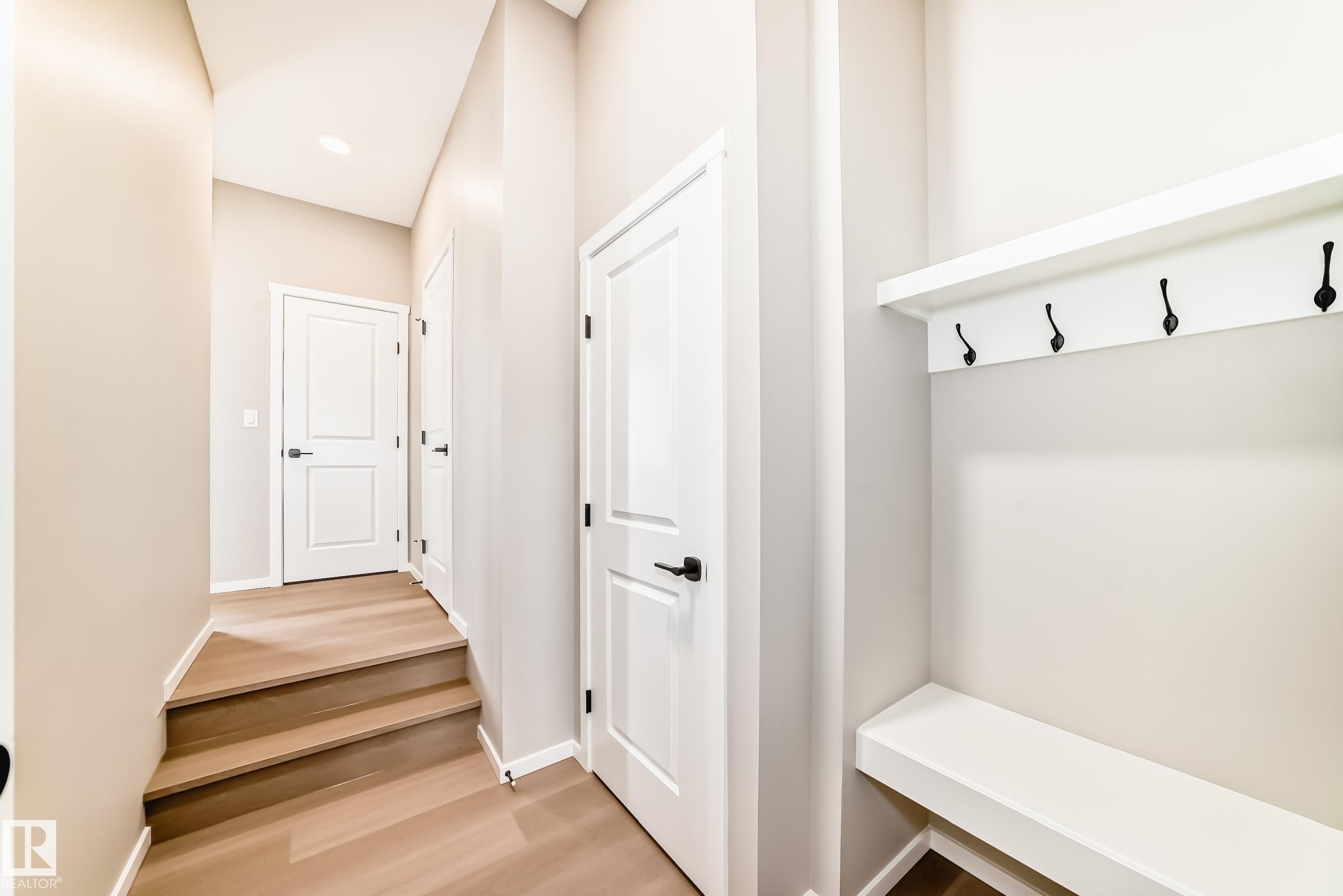 Entryway featuring a built-in bench with integrated coat hooks, recessed lighting, wood-finish flooring, two-panel interior doors, and matte black hardware - 1603 206 Street, Edmonton, AB - Indoor Photo Showing Other Room