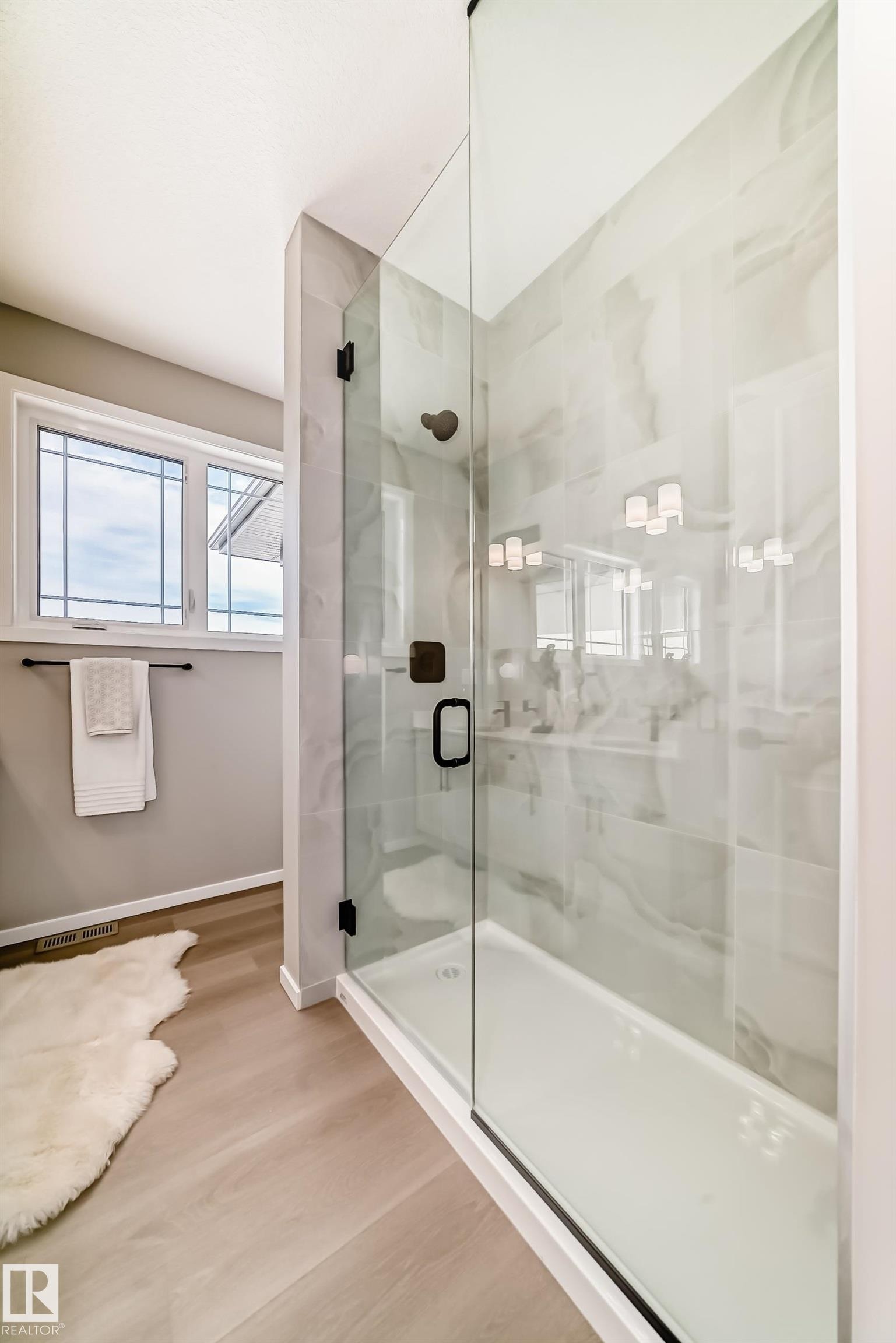 Walk-in shower with clear glass enclosure and matte black hardware, featuring light-toned marble-look tile walls and a white shower pan - 1603 206 Street, Edmonton, AB - Indoor Photo Showing Bathroom