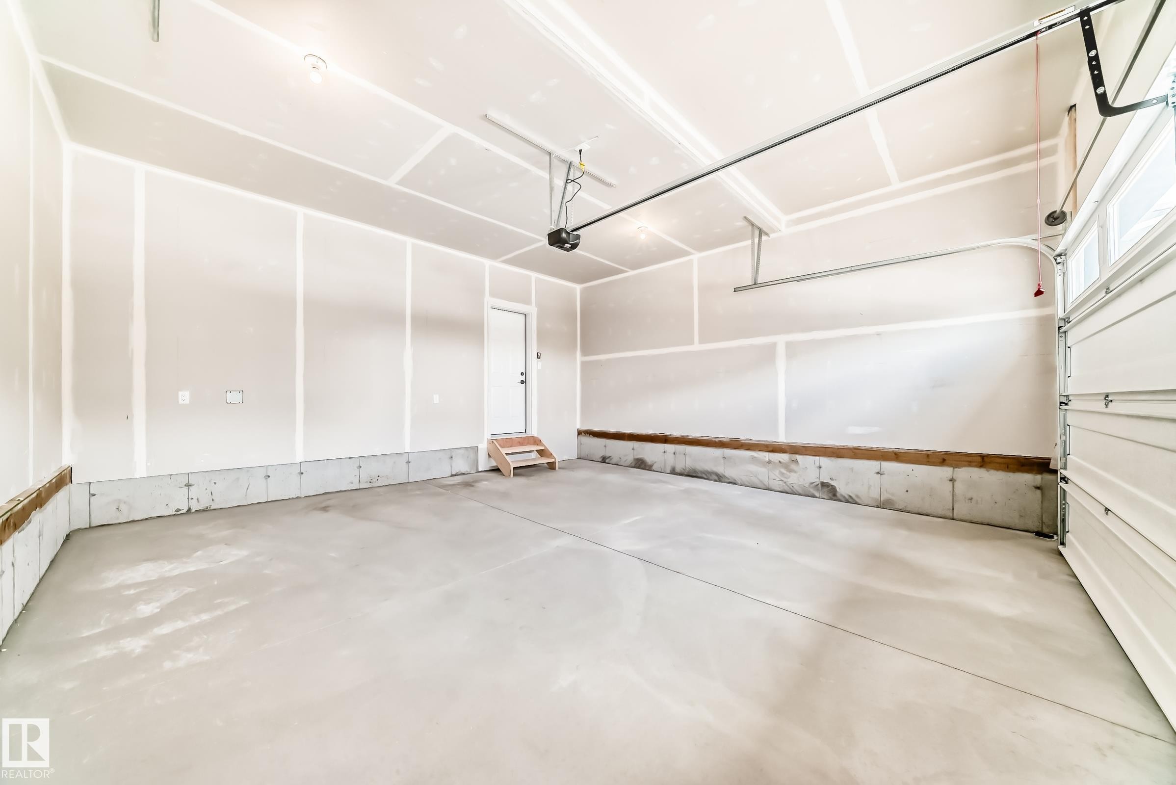 Spacious interior garage featuring a concrete floor, unpainted drywall walls, a white overhead door, and an interior access door with wooden steps - 1603 206 Street, Edmonton, AB - Indoor Photo Showing Garage