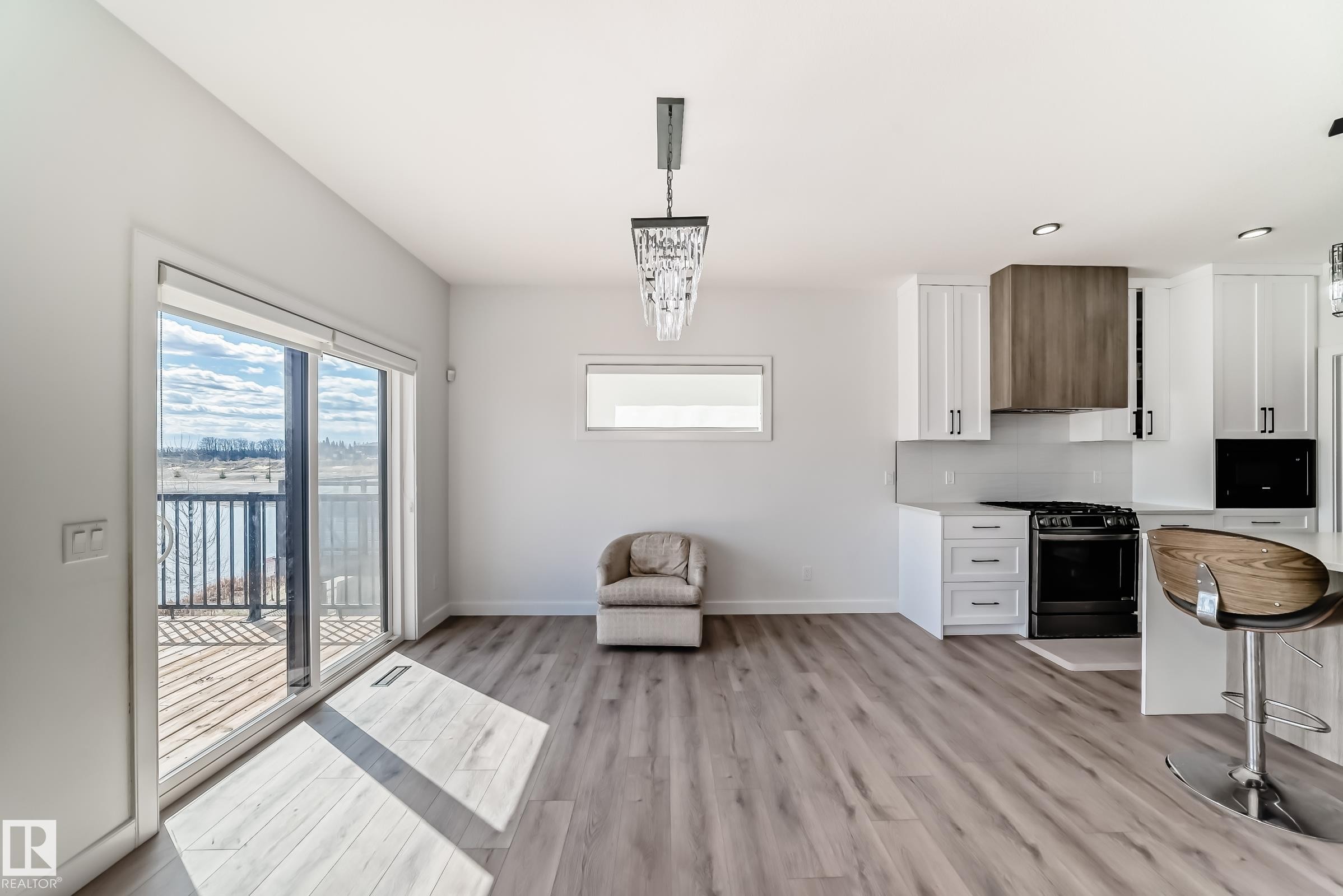 Open-concept living area with wood-finish flooring, a contemporary kitchen, and a sliding glass door to a deck - 3247 Chernowski Way, Edmonton, AB - Indoor