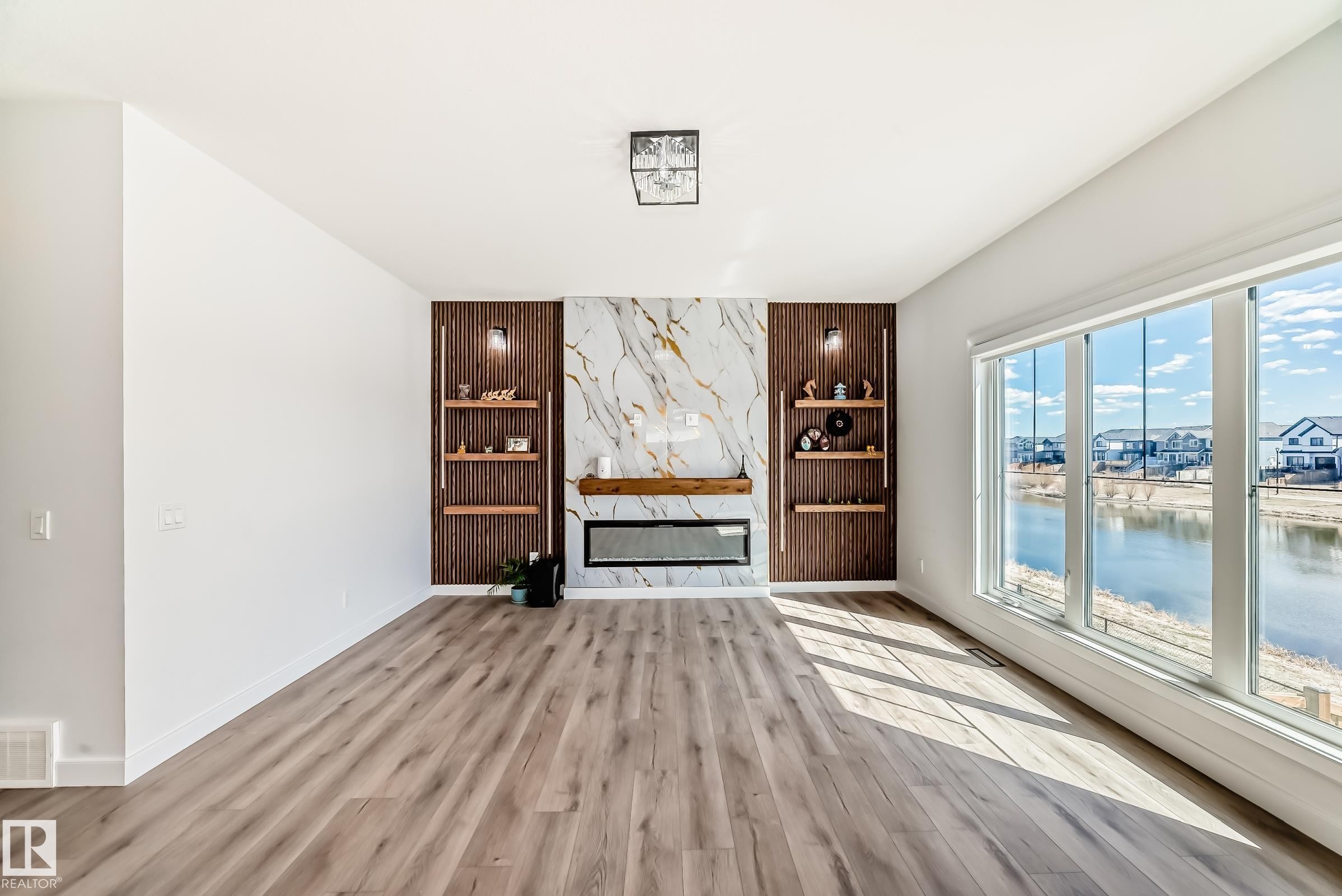 Living area featuring wood-finish flooring and expansive windows overlooking a body of water - 3247 Chernowski Way, Edmonton, AB - Indoor Photo Showing Other Room