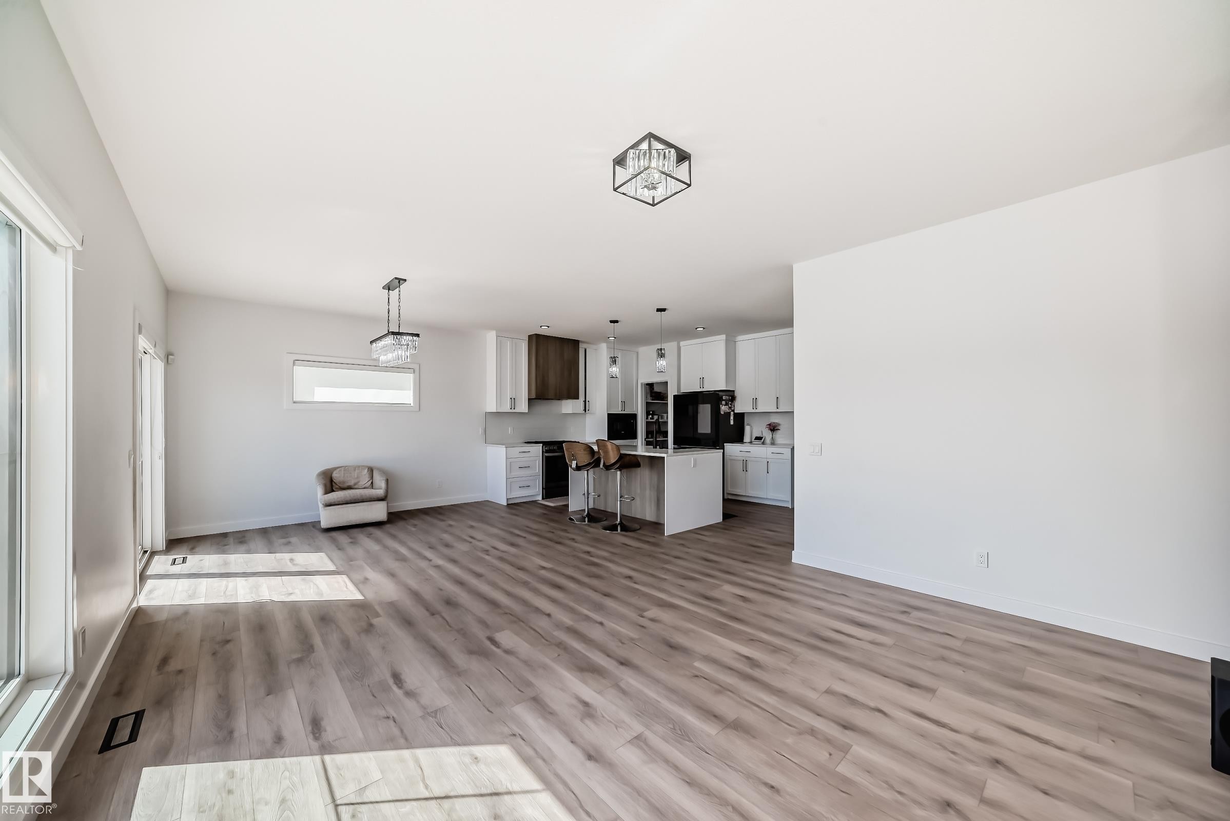 Spacious open-concept living area featuring wood-finish flooring, large windows, and a contemporary kitchen - 3247 Chernowski Way, Edmonton, AB - Indoor