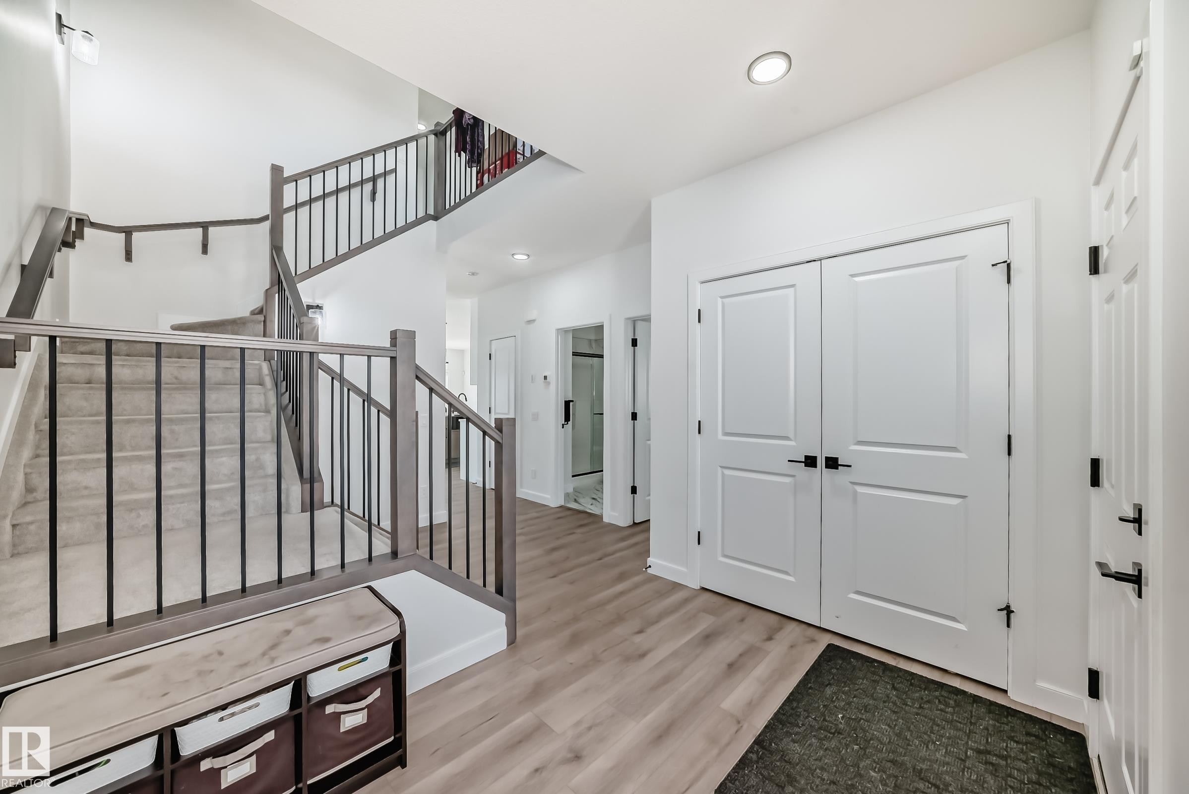 Entryway featuring light wood-finish flooring, white panel doors with matte black hardware, and a staircase with gray balusters and handrails - 3247 Chernowski Way, Edmonton, AB - Indoor Photo Showing Other Room