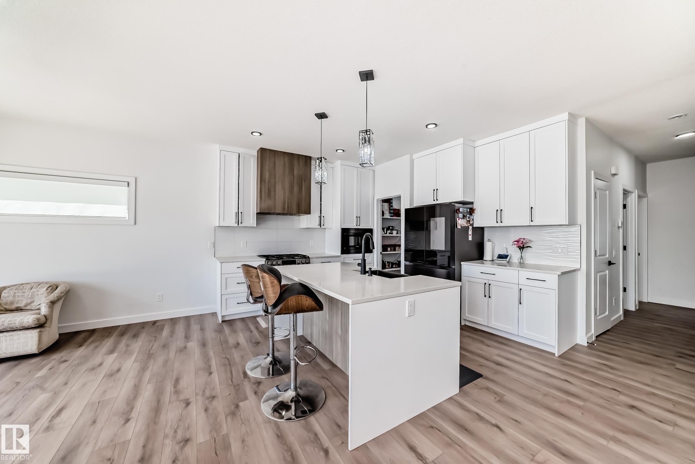 Open-concept kitchen featuring white shaker cabinetry, an expansive center island, integrated black appliances, a wood-finish range hood, and plank wood-finish flooring - 3247 Chernowski Way, Edmonton, AB - Indoor Photo Showing Kitchen