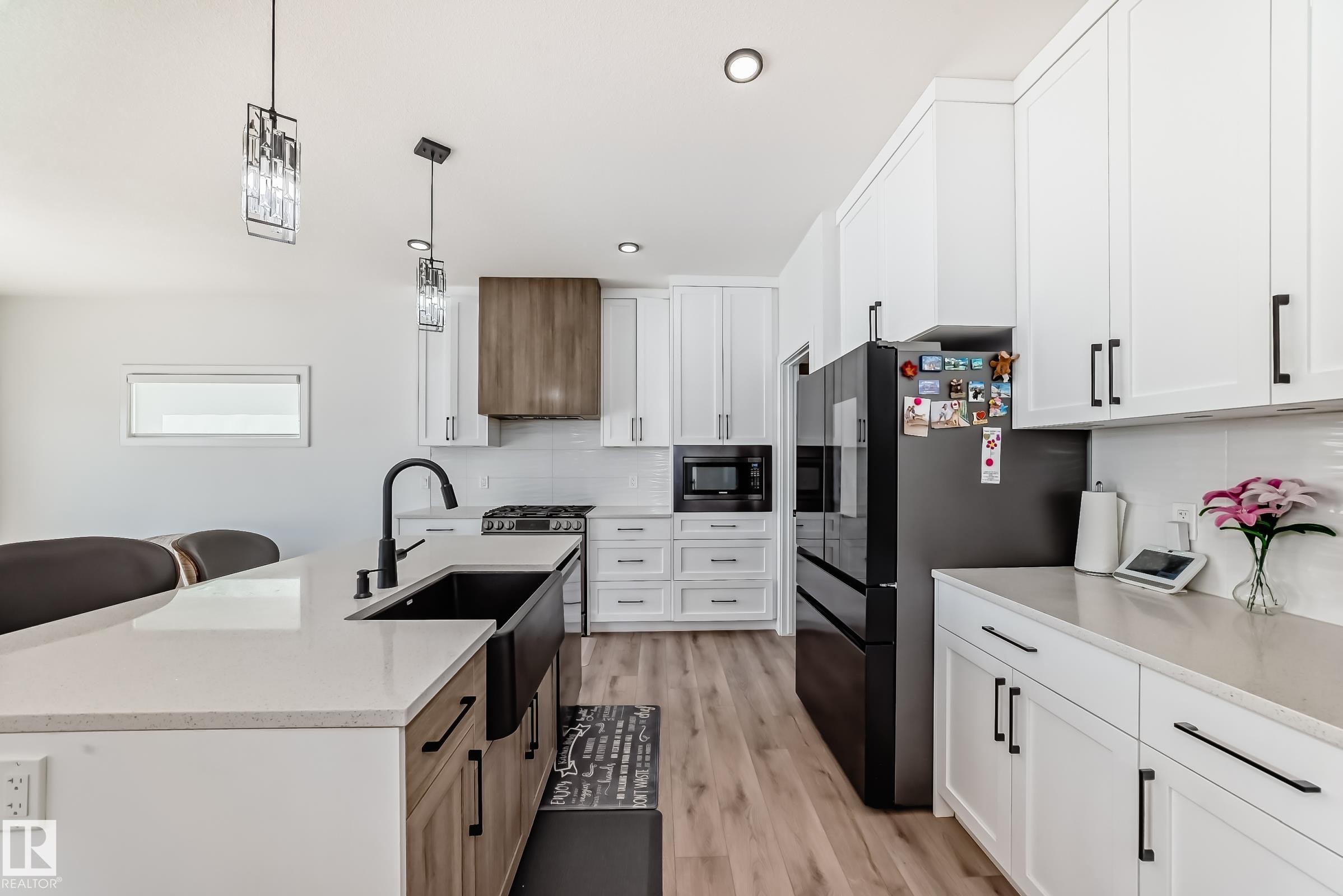 Modern kitchen featuring white shaker cabinetry, light wood-finish flooring, and a large central island with a black farmhouse sink - 3247 Chernowski Way, Edmonton, AB - Indoor Photo Showing Kitchen With Upgraded Kitchen