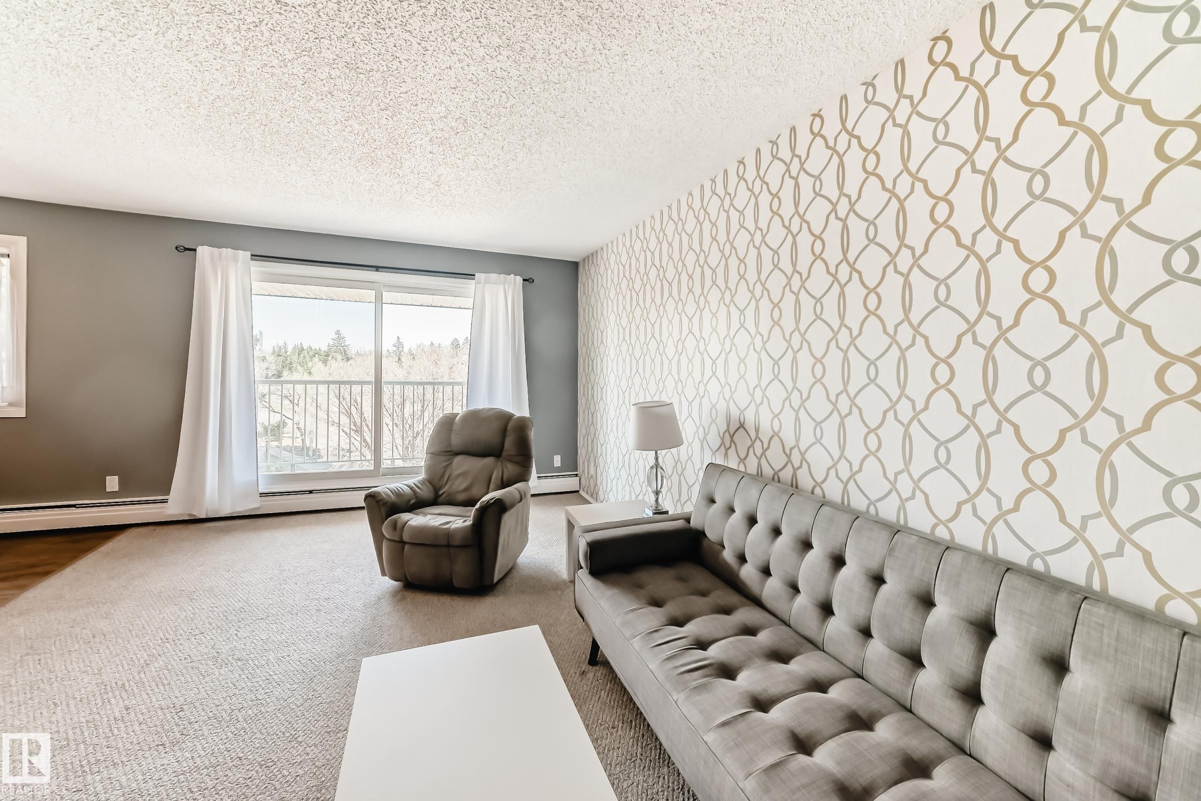 Living area featuring a patterned accent wall and large sliding glass doors opening to a balcony - 423 5125 Riverbend Road, Edmonton, AB - Indoor